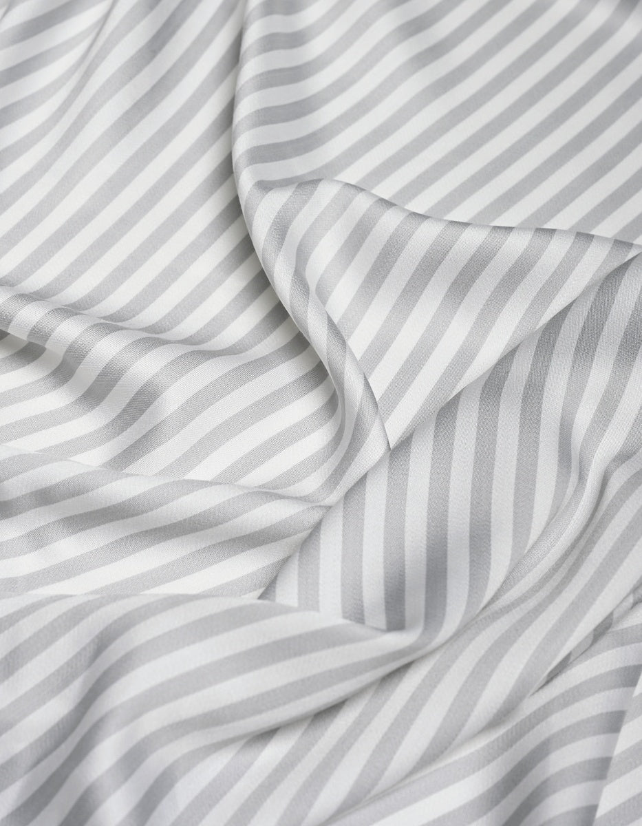 The Cozy Earth Bamboo Flat Sheet features a white fabric with diagonal light gray stripes that drape softly, forming gentle folds and shadows. The consistent pattern and smooth, silky texture enhance its luxurious feel.