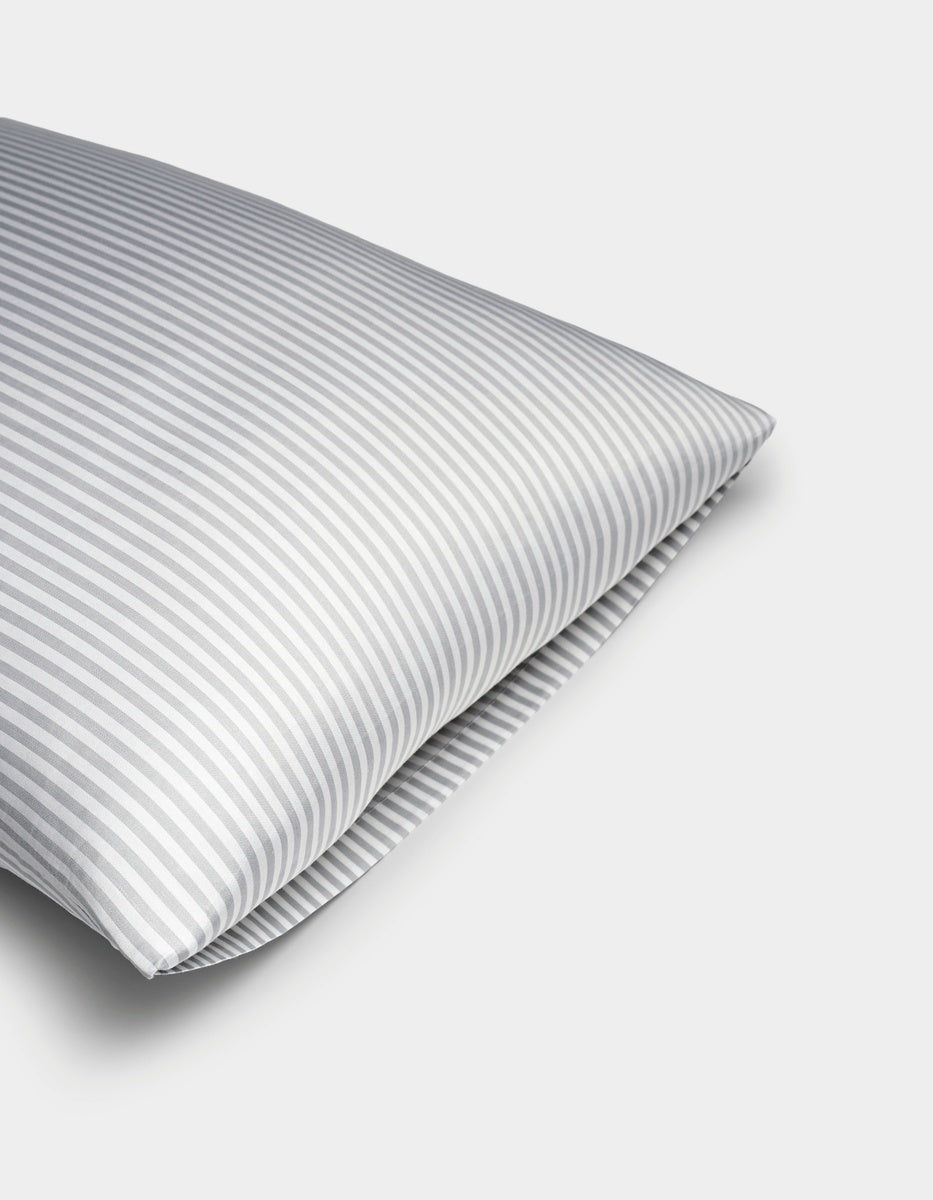 A close-up of a Bamboo Pillowcase by Cozy Earth, featuring gray and white vertical stripes, set against a plain white background.