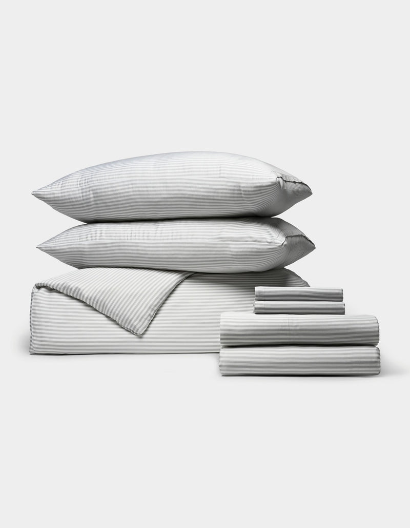 A neatly stacked set of Cozy Earth’s Bamboo Bedding Ultimate Bundle, featuring two pillows, a folded comforter, and two stacks of folded sheets in gray and white stripes, displayed on a light gray background.