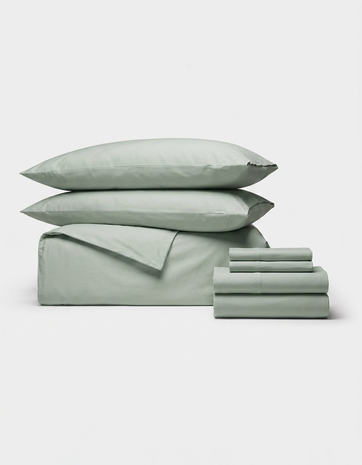The Cozy Earth Soft-Wash Cotton Bedding Core Bundle, in sage green, features two pillows, a duvet cover, a flat sheet, and fitted sheets neatly folded on a plain white background.