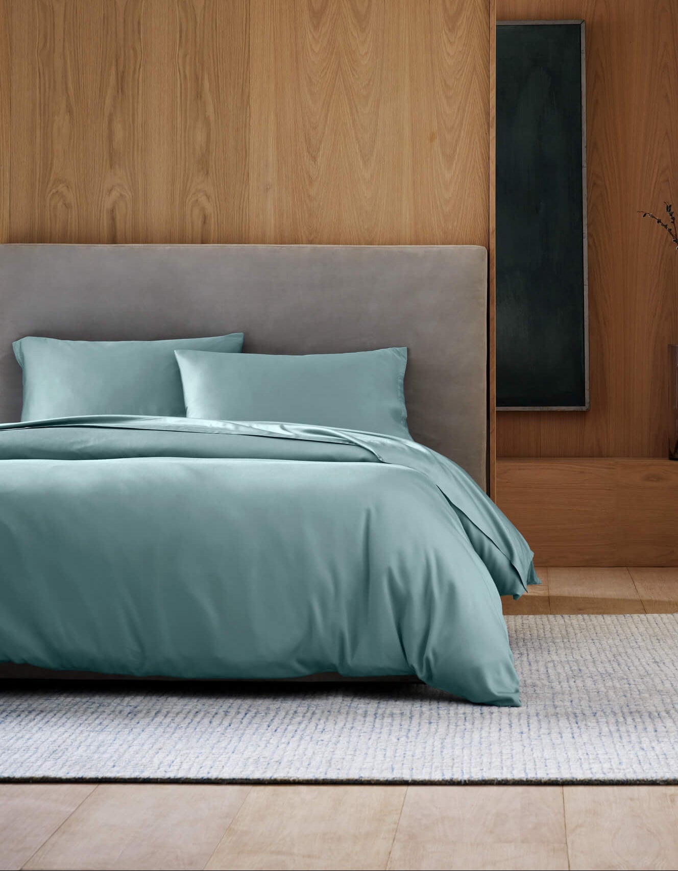 A modern bedroom showcases the Cozy Earth Bamboo Bedding Deluxe Bundle in light teal, paired with a gray upholstered headboard, a light rug, and minimalist wood-paneled walls.