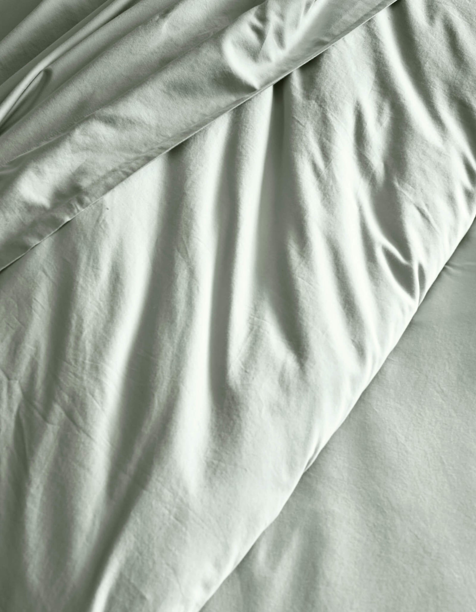 The Soft-Wash Cotton Duvet Cover by Cozy Earth features a light gray finish with subtle wrinkles and gentle folds, creating soft shadows across the fabric.