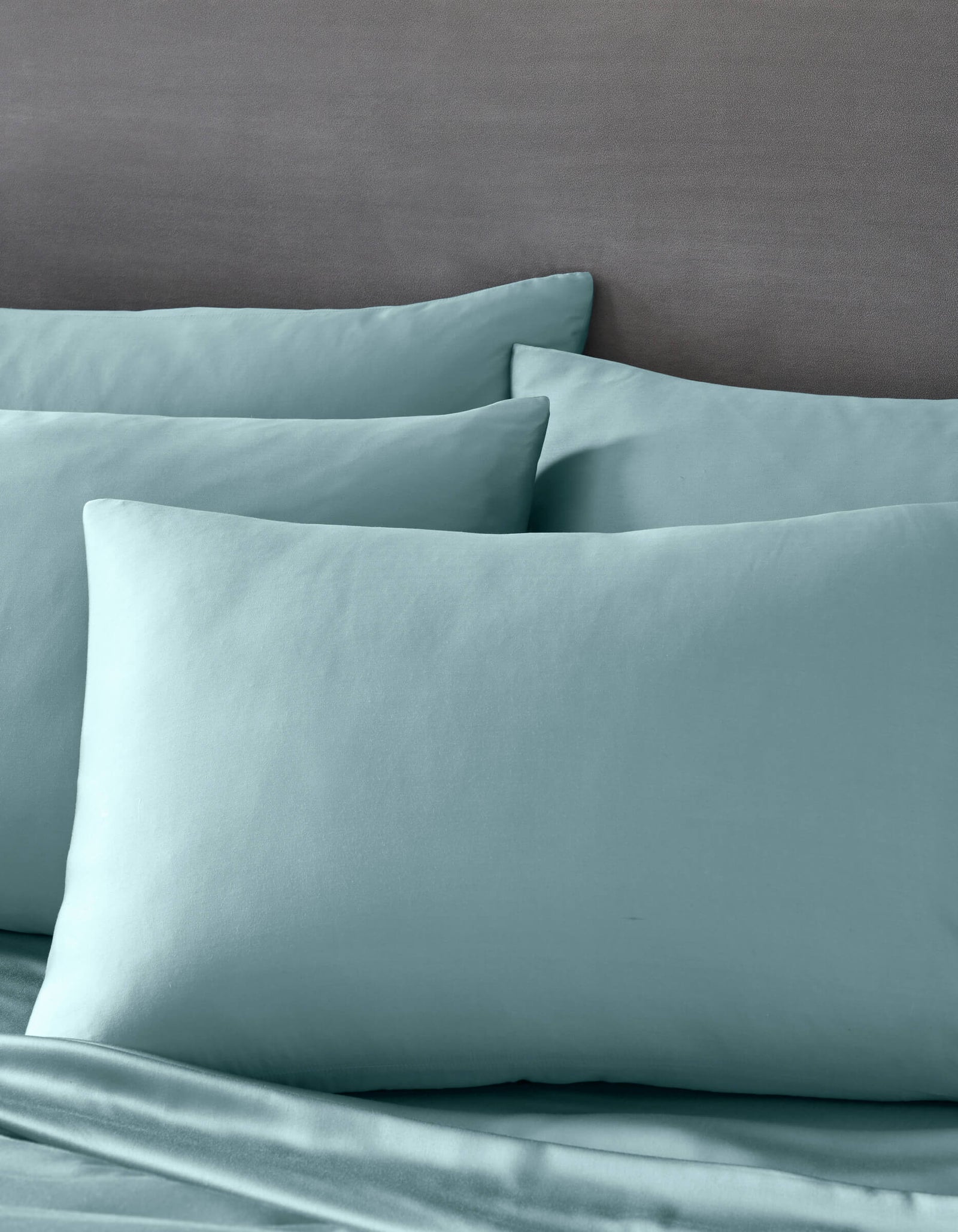 Cozy Earth's Bamboo Pillowcases in light blue are paired with matching bedsheets on a bed with a gray headboard, creating a calm and inviting atmosphere.