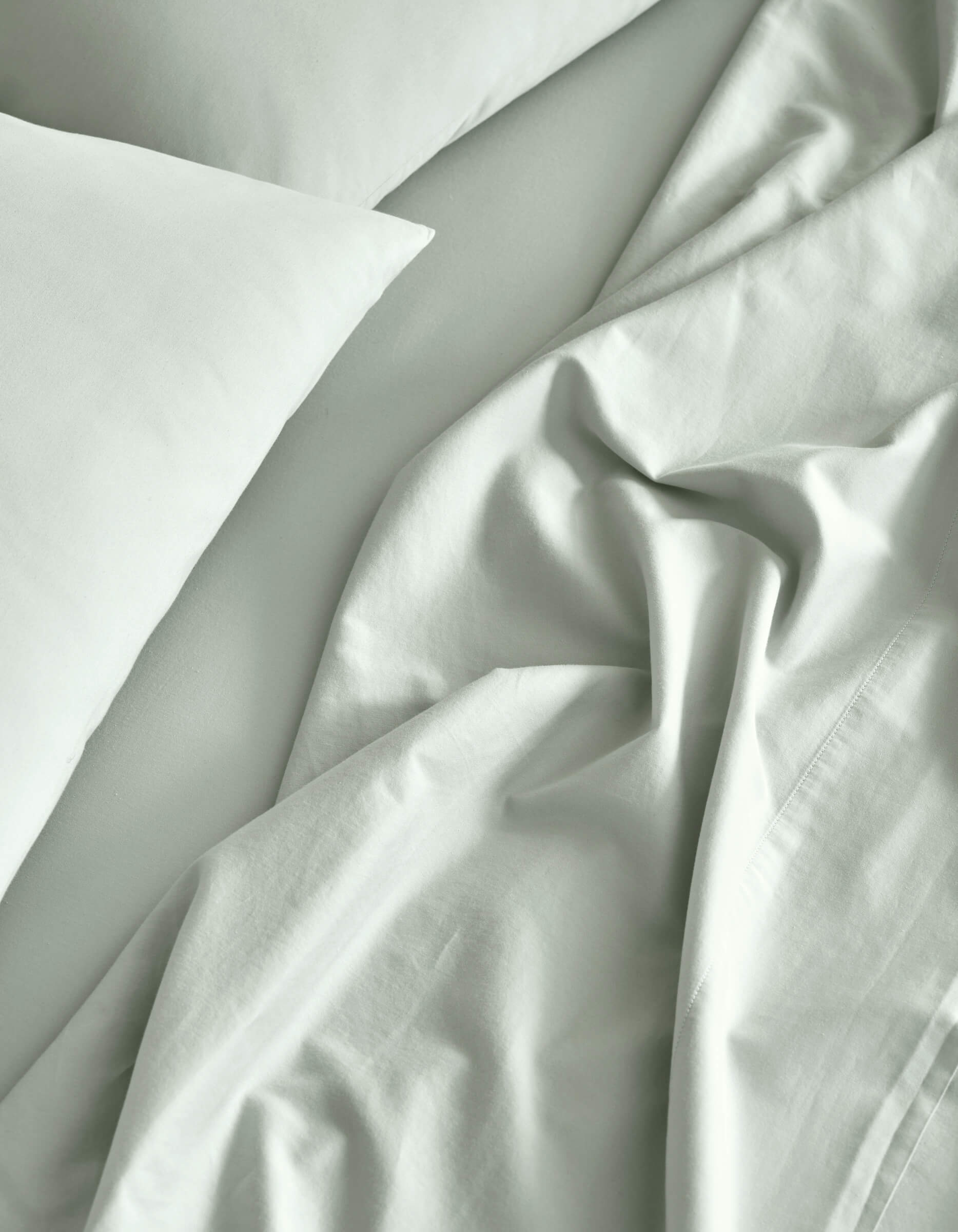 A close-up of a neatly made bed features the Cozy Earth Soft-Wash Cotton Sheet Set in light gray, with slightly rumpled sheets and pillowcases creating soft folds and natural shadows.