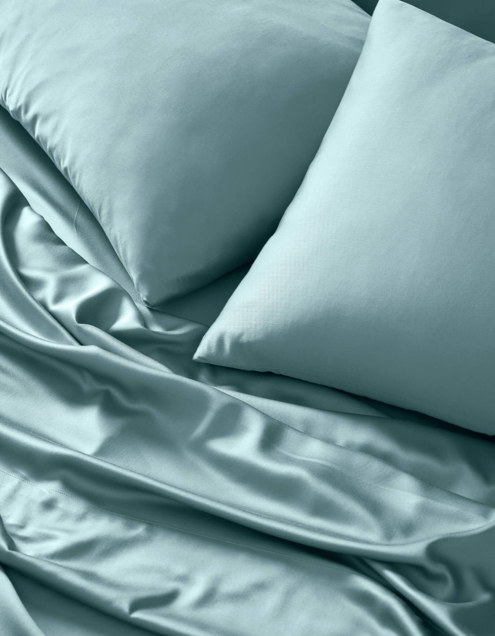 A close-up of Cozy Earth's Bamboo Sheet Set in light blue, neatly arranged with two matching pillows. The smooth, soft fabric shows subtle folds and a gentle sheen for an inviting look.