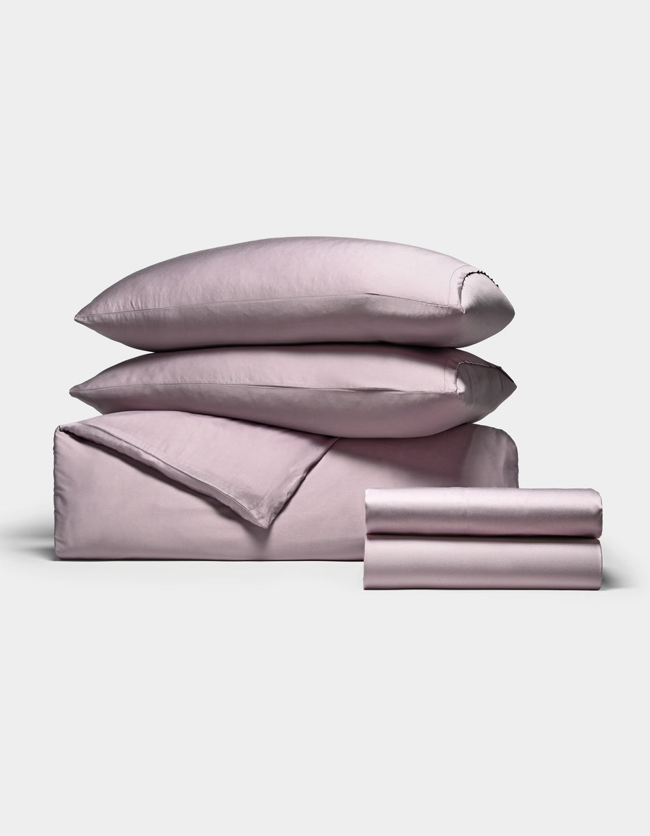 The Cozy Earth Bamboo Bedding Deluxe Bundle, in lavender, includes two pillows, a duvet, and sheets neatly folded and displayed on a plain white background.