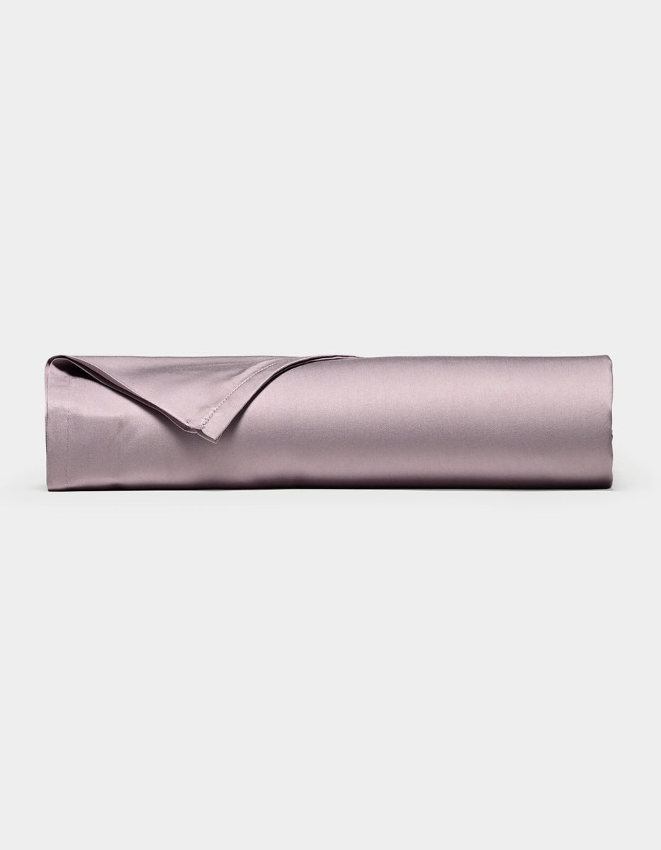 A neatly rolled, lavender-colored Bamboo Flat Sheet by Cozy Earth, with one corner folded over, displayed against a plain white background.