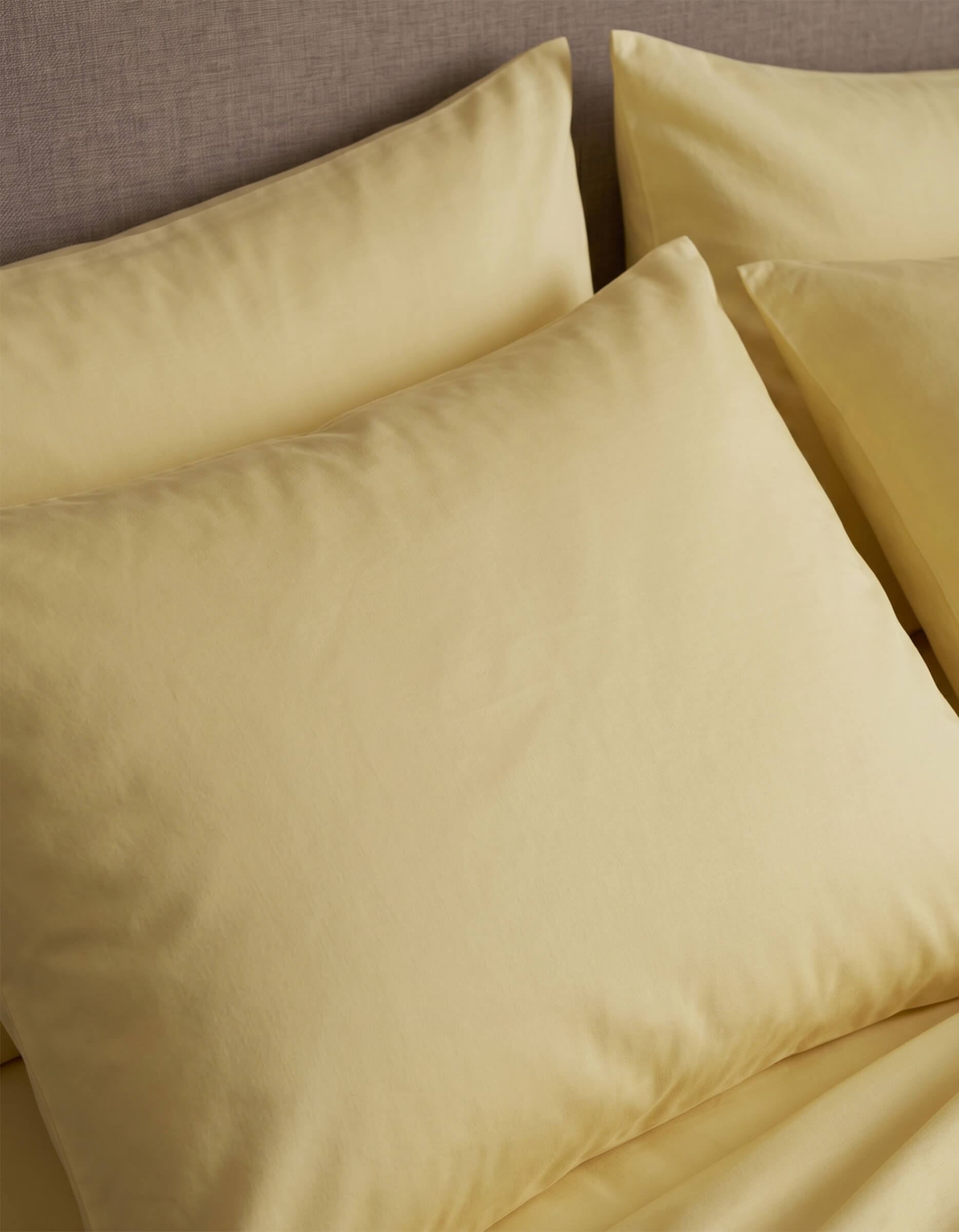 Close-up of neatly arranged Cozy Earth Bamboo Jersey Pillowcases in pale yellow on a bed with a beige upholstered headboard.