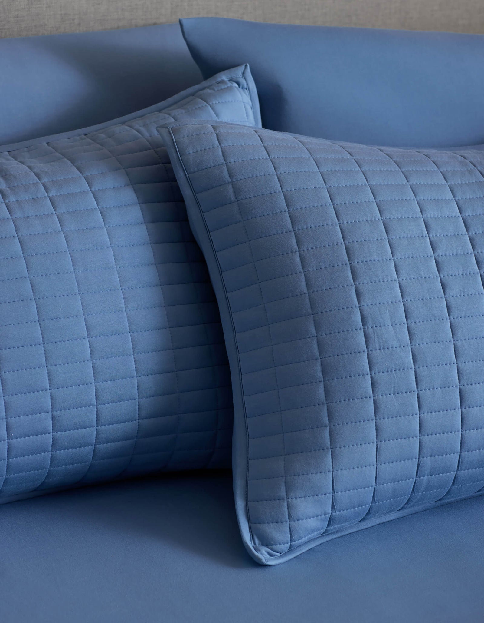 Two Bamboo Jersey Quilted Shams by Cozy Earth, featuring a blue grid pattern, rest on a matching surface for a calm, coordinated look.