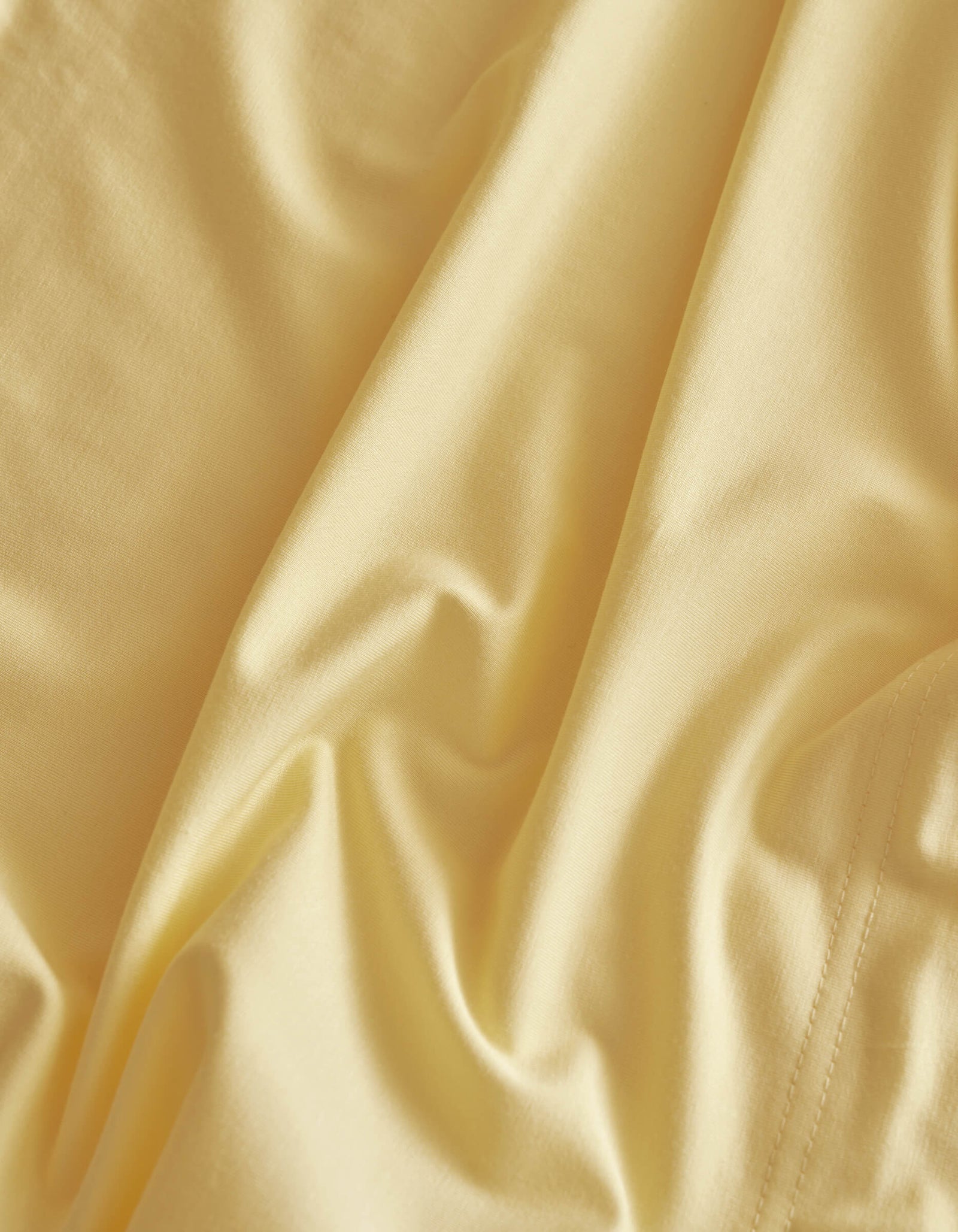 A close-up of Cozy Earth's Bamboo Jersey Sheet Set in soft, light yellow shows gentle folds, subtle shadows, and highlights its smooth texture with a slight sheen.