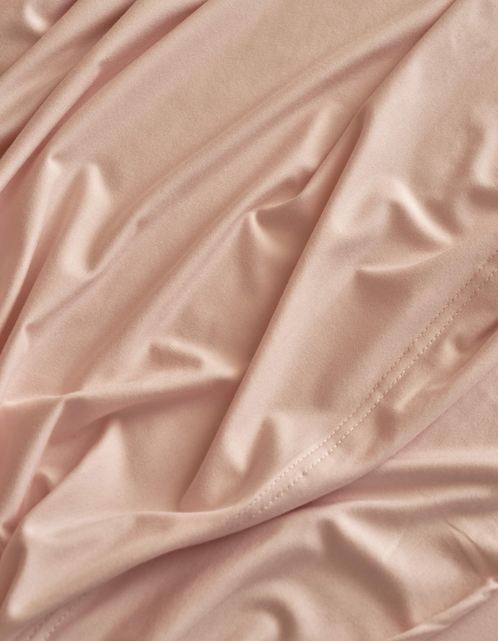 Close-up of Cozy Earth Bamboo Jersey Sheet Set in light pink, featuring smooth, shiny texture with soft folds, gentle wrinkles, and subtle edge stitching.