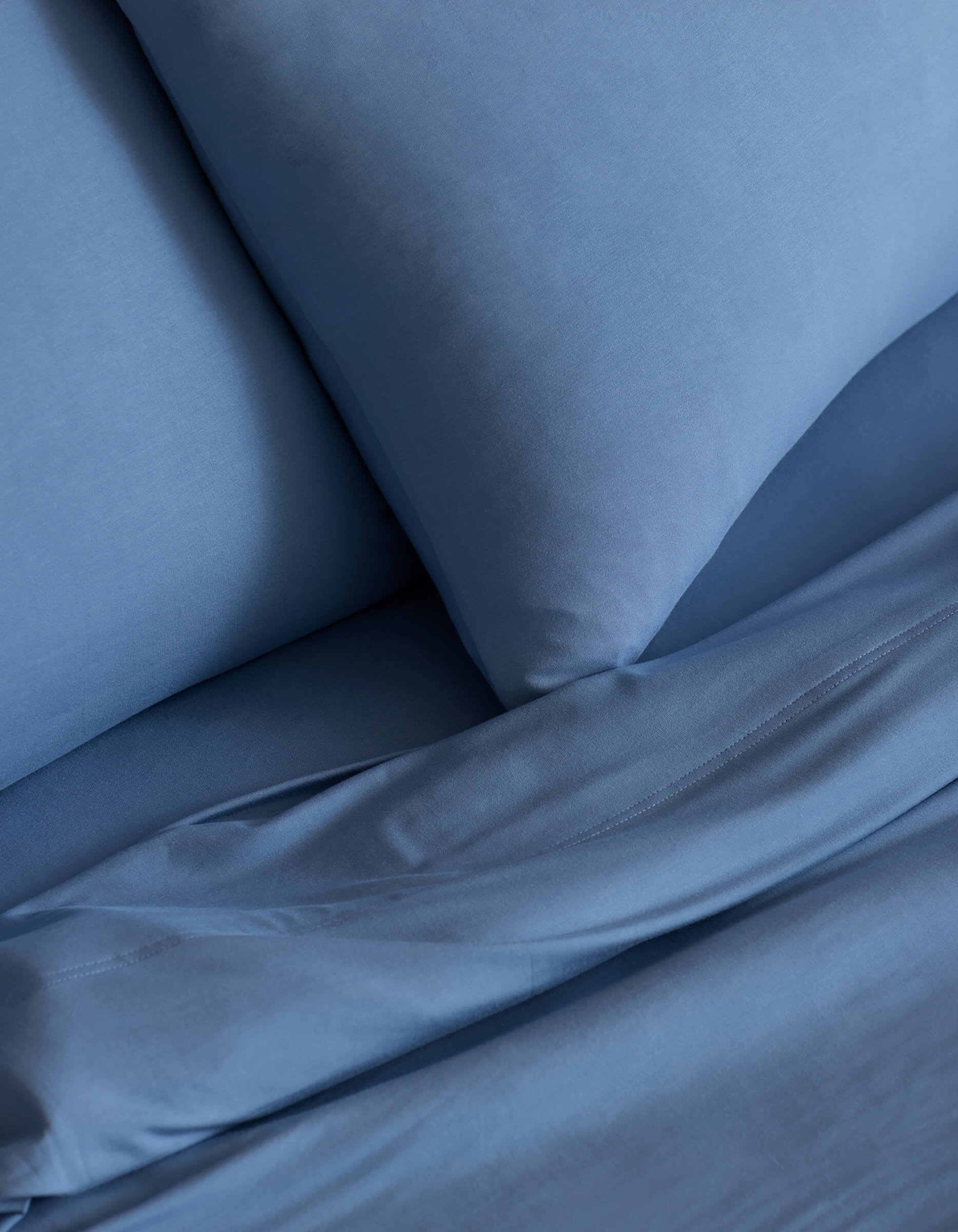 Close-up of the Cozy Earth Bamboo Jersey Sheet Set in blue, featuring smooth fabric texture and tidy folds on a neatly made bed with matching pillowcases.
