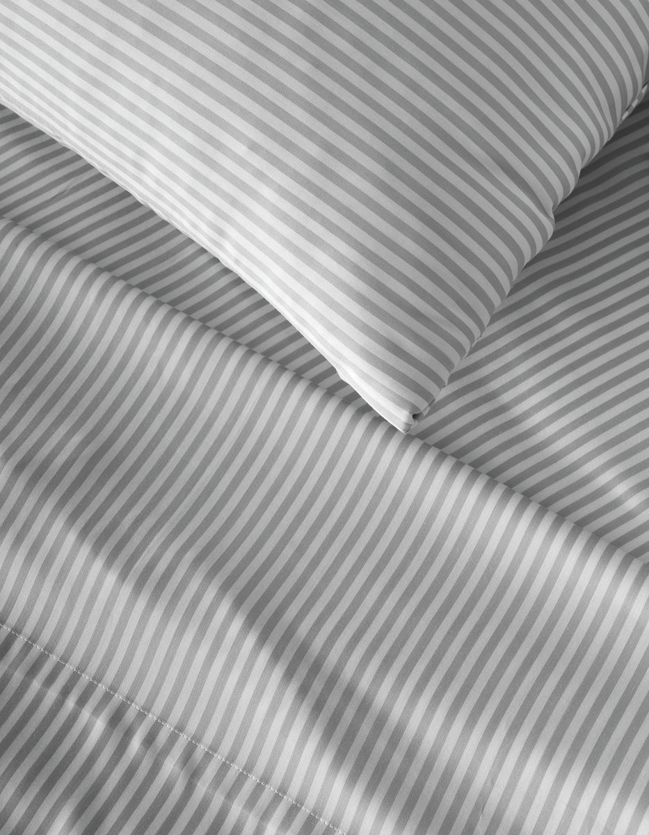Close-up of a bed with a pillow and sheets featuring the Bamboo Flat Sheet from Cozy Earth in a gray and white diagonal stripe pattern.
