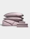 A neatly stacked set of Cozy Earth’s Bamboo Bedding Ultimate Bundle, featuring two pillows, a folded duvet, a flat sheet, and several smaller folded sheets in pale pink, all arranged against a plain white background.|Color:Lavender
