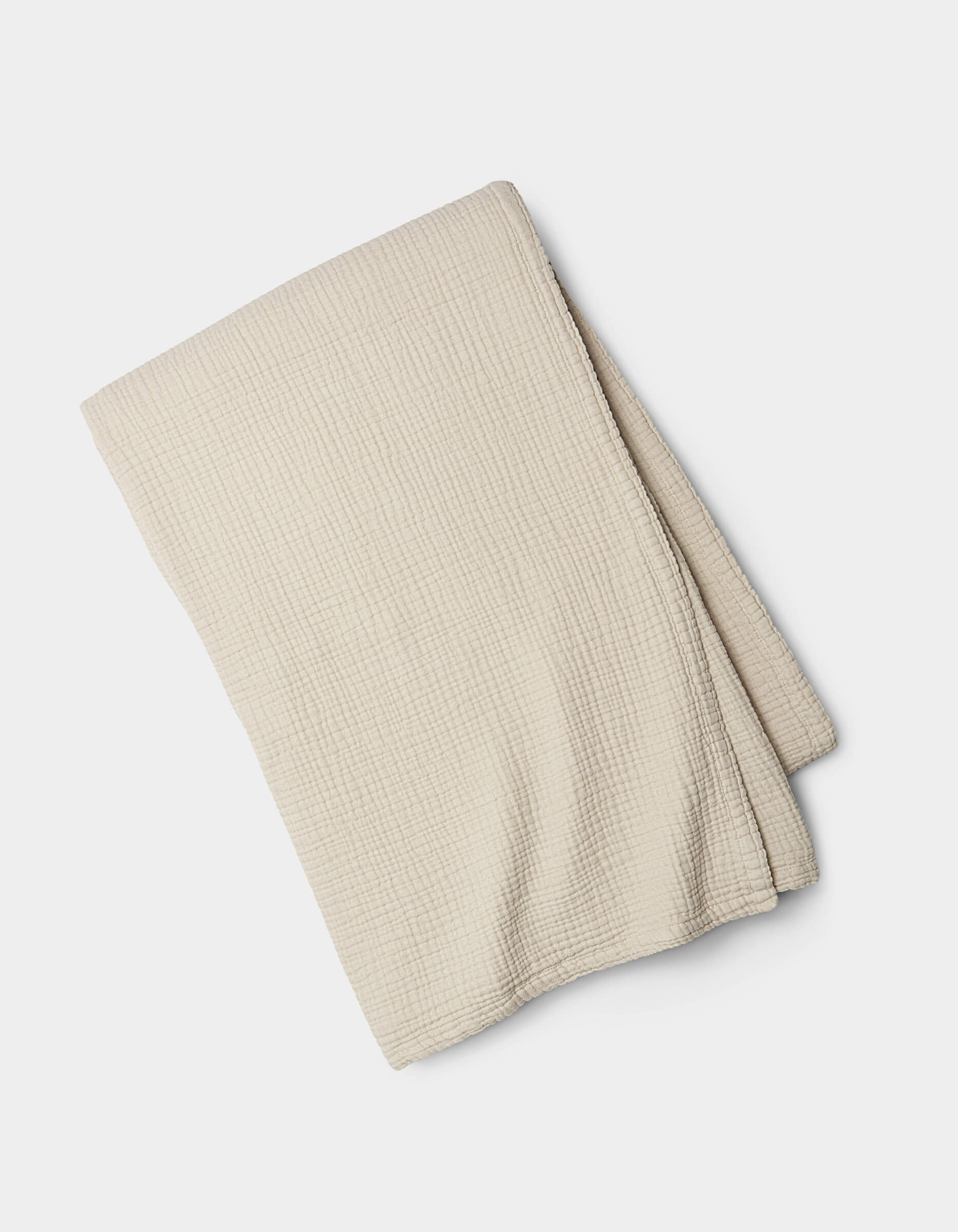 The Cozy Earth Cotton Gauze Blanket, light beige with a subtle grid texture, is neatly folded and displayed on a white background.