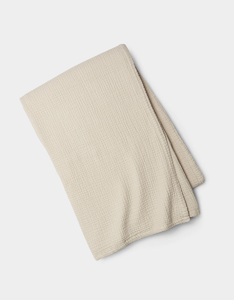 The Cozy Earth Cotton Gauze Blanket, light beige with a subtle grid texture, is neatly folded and displayed on a white background.