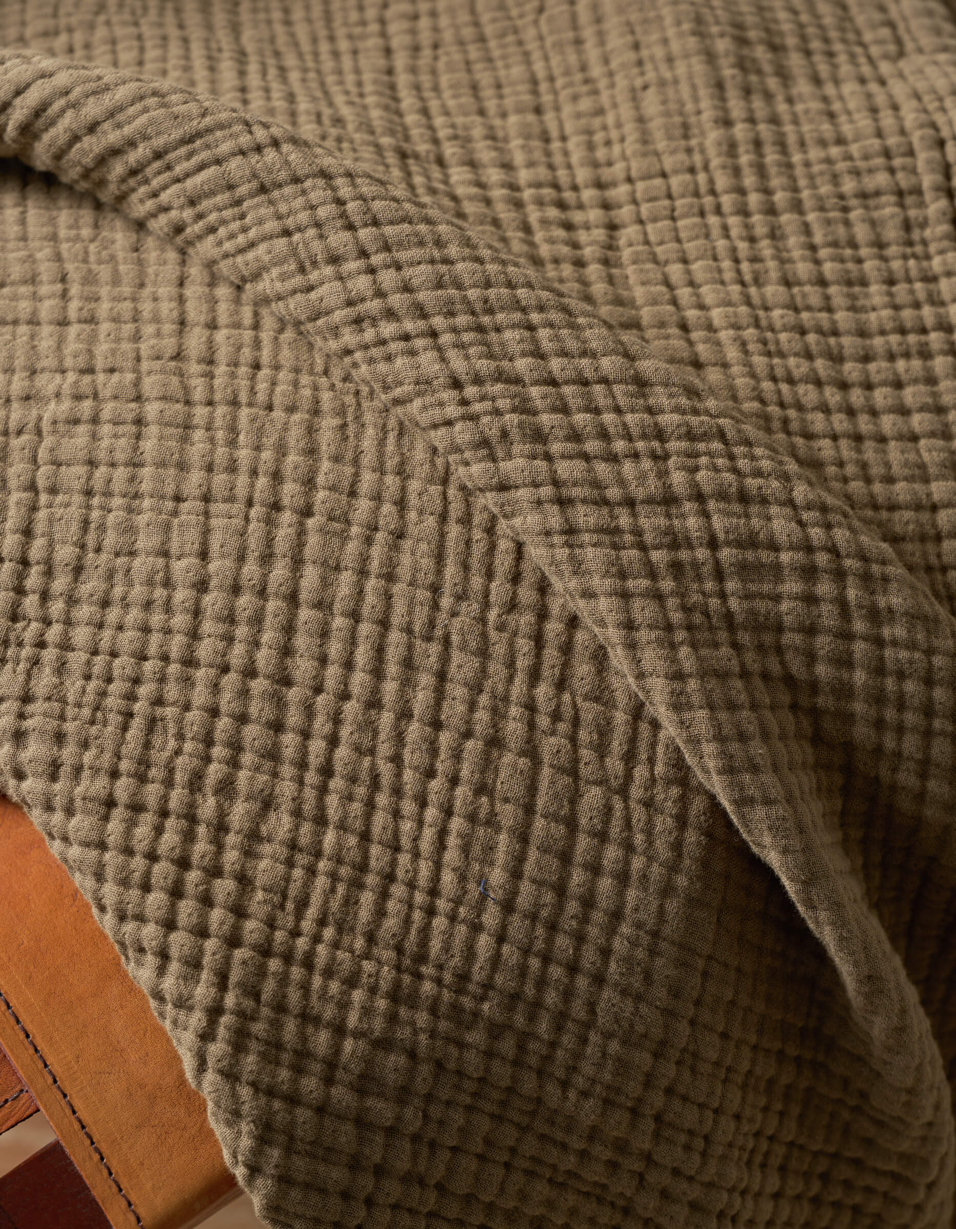A close-up of the Cozy Earth Cotton Gauze Blanket, draped over a surface, highlights its soft, quilted texture and grid-like pattern for a cozy look.