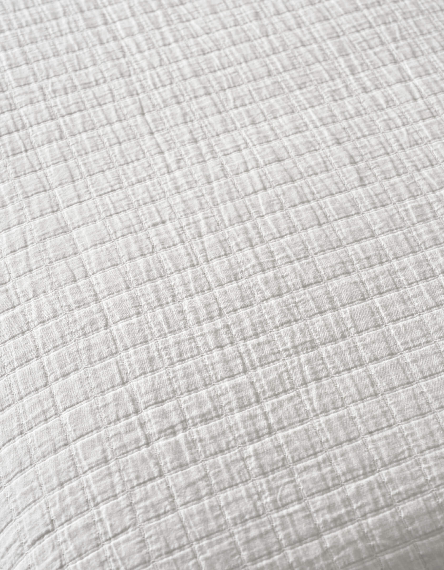 A close-up of Cozy Earth's Waterfront Grid Matelasse Blanket, featuring white fabric with a subtle checkered texture, small raised squares, and soft, crinkled material.