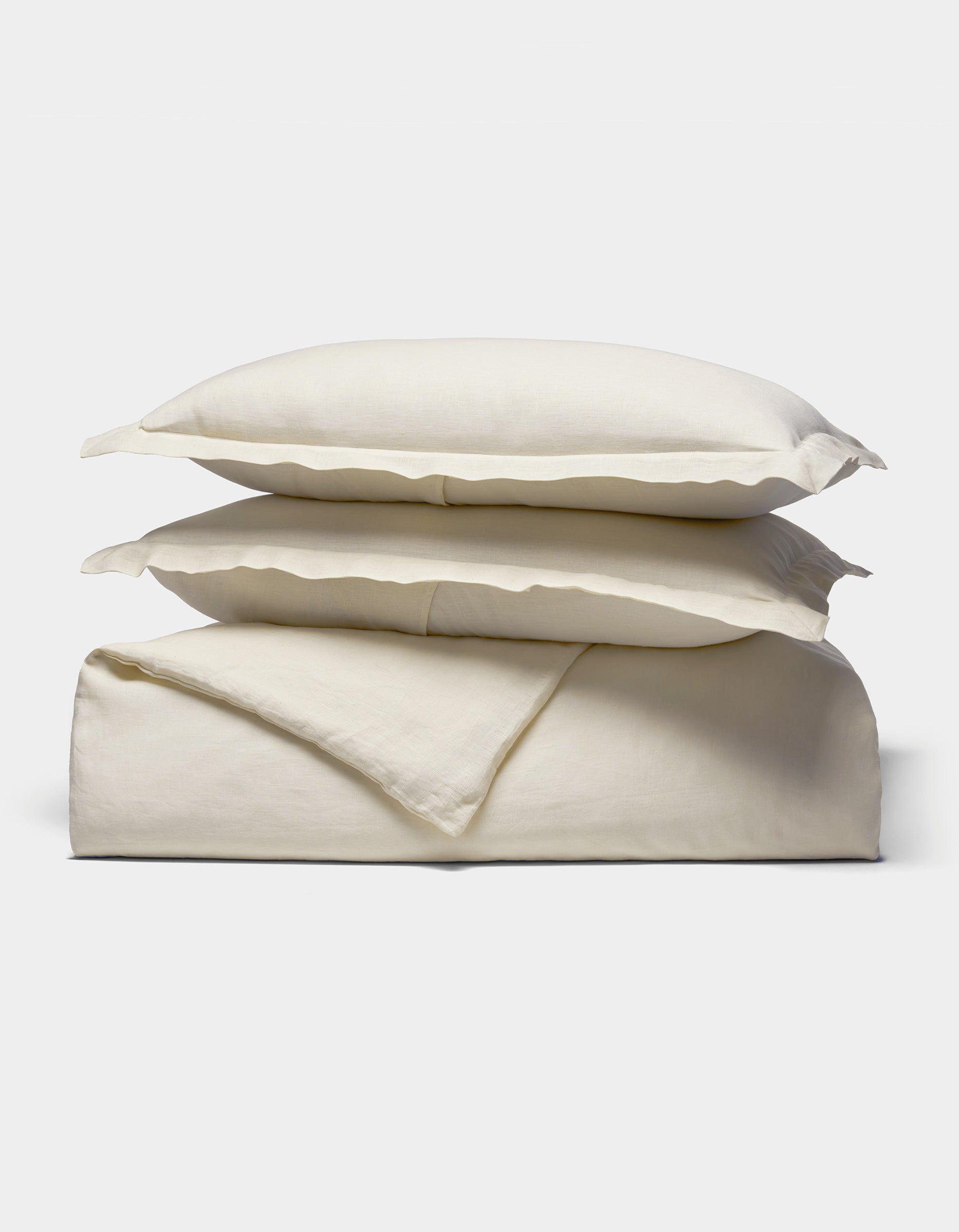 The Cozy Earth Linen Duvet Set features cream-colored, soft and smooth bedding—two pillows stacked atop a folded duvet—displayed against a plain white background.