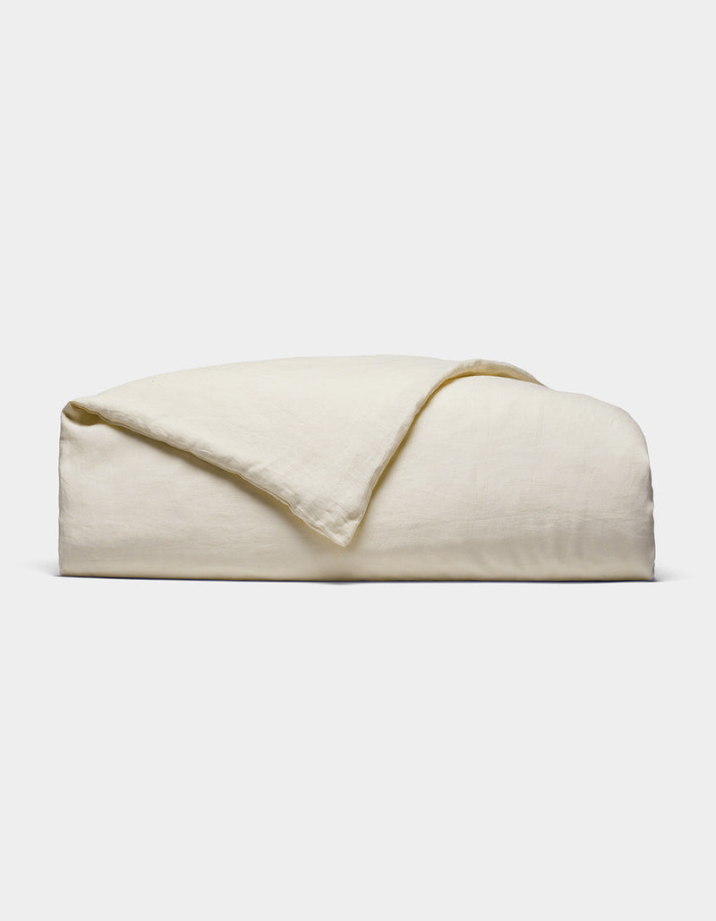 The Cozy Earth Linen Duvet Cover, in an off-white shade, is neatly folded against a white background. Its soft, slightly textured fabric is visible with one corner casually turned over.