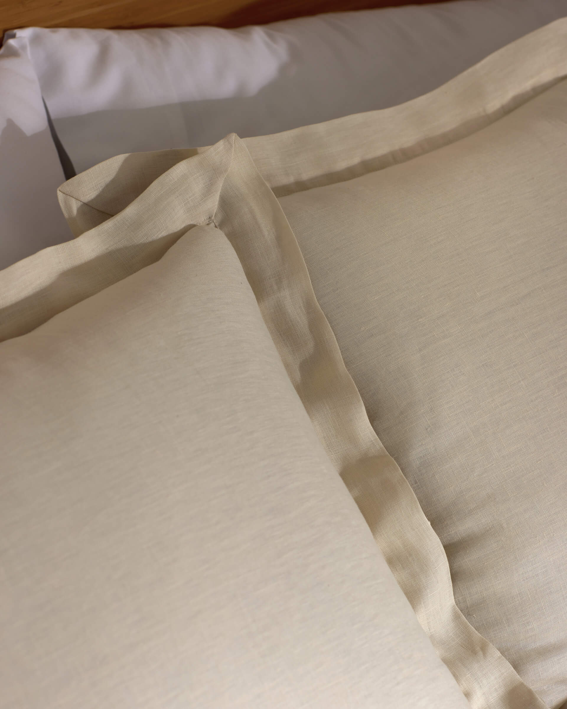 Close-up of two Cozy Earth Linen Shams in beige with subtle texture and flange edges, arranged neatly on a matching bed sheet. The bedding looks soft and inviting.