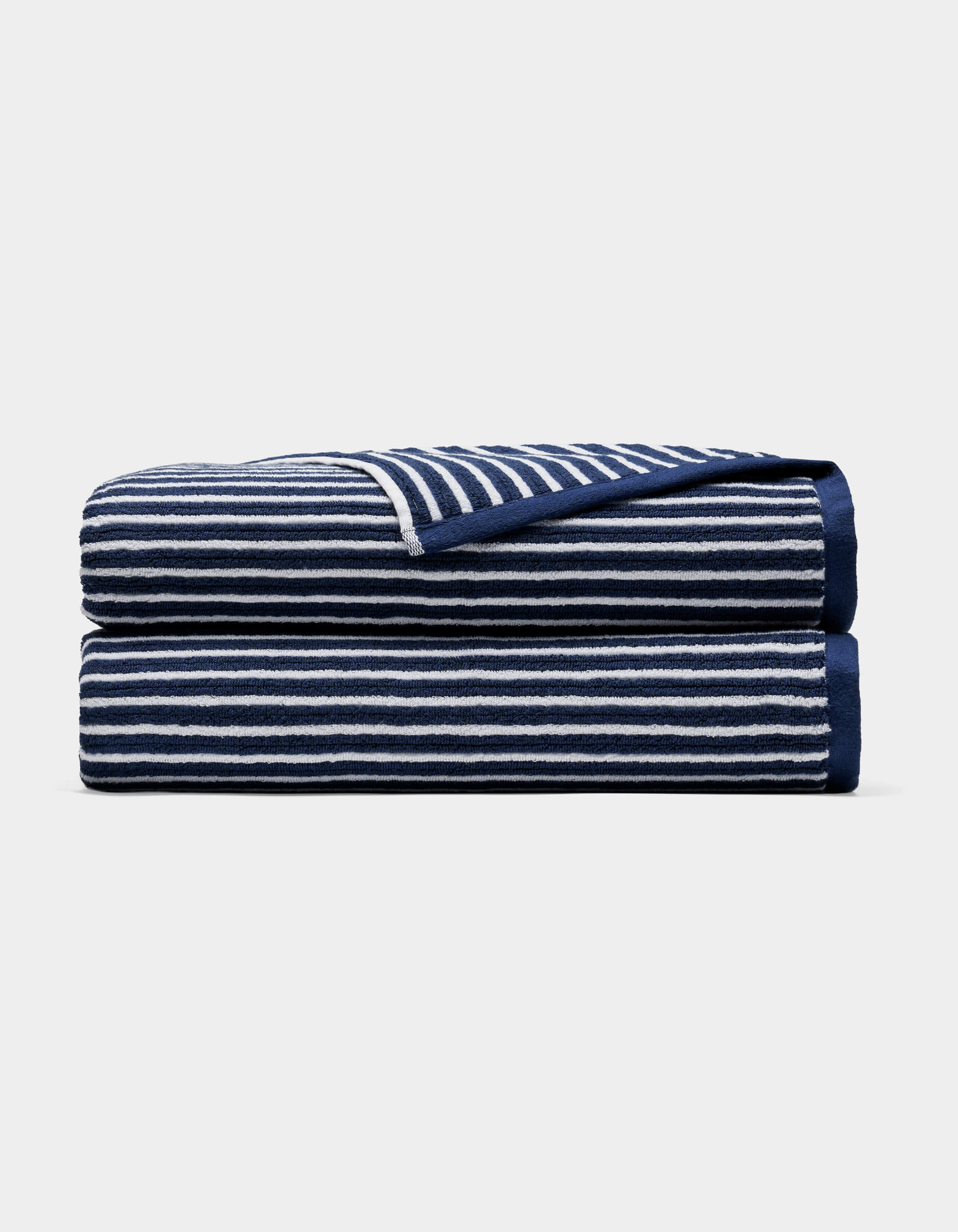 A Cozy Earth Ribbed Terry Bath Sheet in navy blue with horizontal white stripes, neatly folded and stacked on a plain light background.|Color:Obsidian Stripe