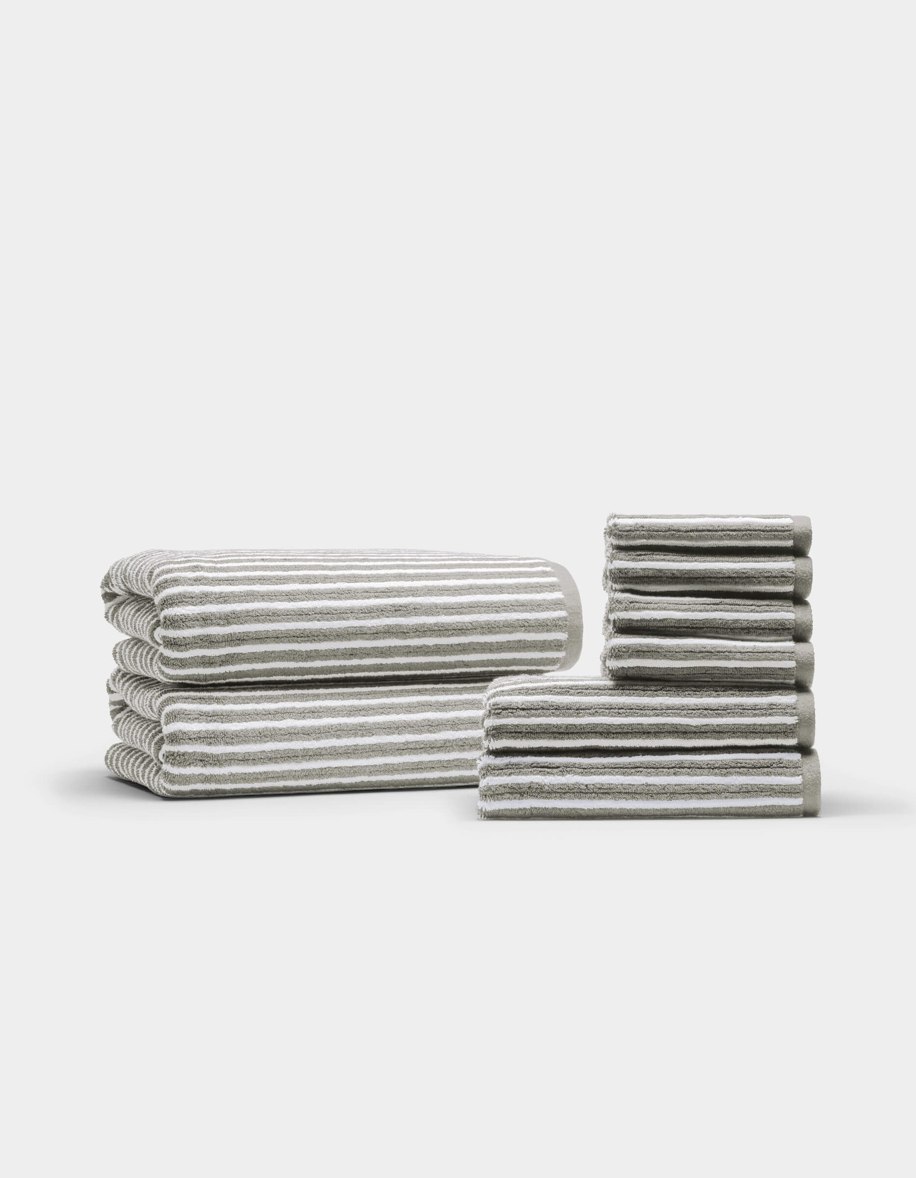 Two neatly arranged stacks of the Cozy Earth Ribbed Terry Bath Towel Set are displayed on a plain white background—one larger stack featuring bath towels, and a smaller stack showcasing hand towels and washcloths.|Color:Dew Stripe