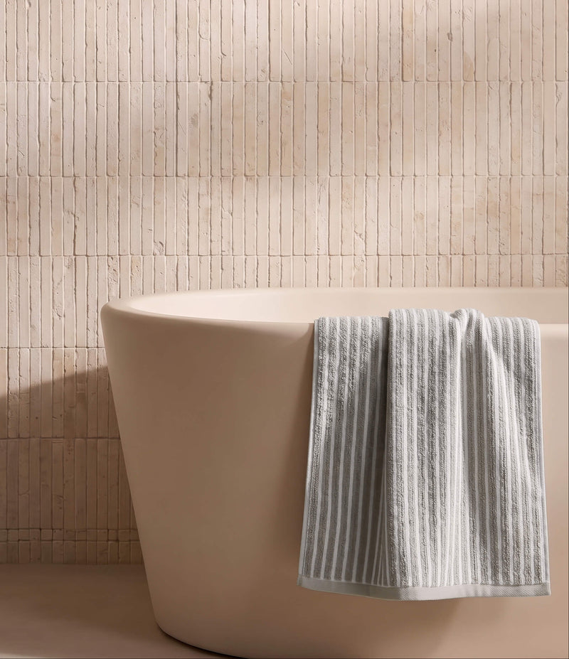 A beige freestanding bathtub with a Cozy Earth Ribbed Terry Bath Towel draped over the side, set against a light tan tiled wall.