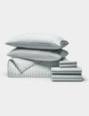 A neatly arranged stack of Cozy Earth's Soft-Wash Cotton Bedding Core Bundle, including pillows, a comforter, and folded sheets in white and light blue, displayed on a plain white background.|Color:River and Sea Salt Stripe