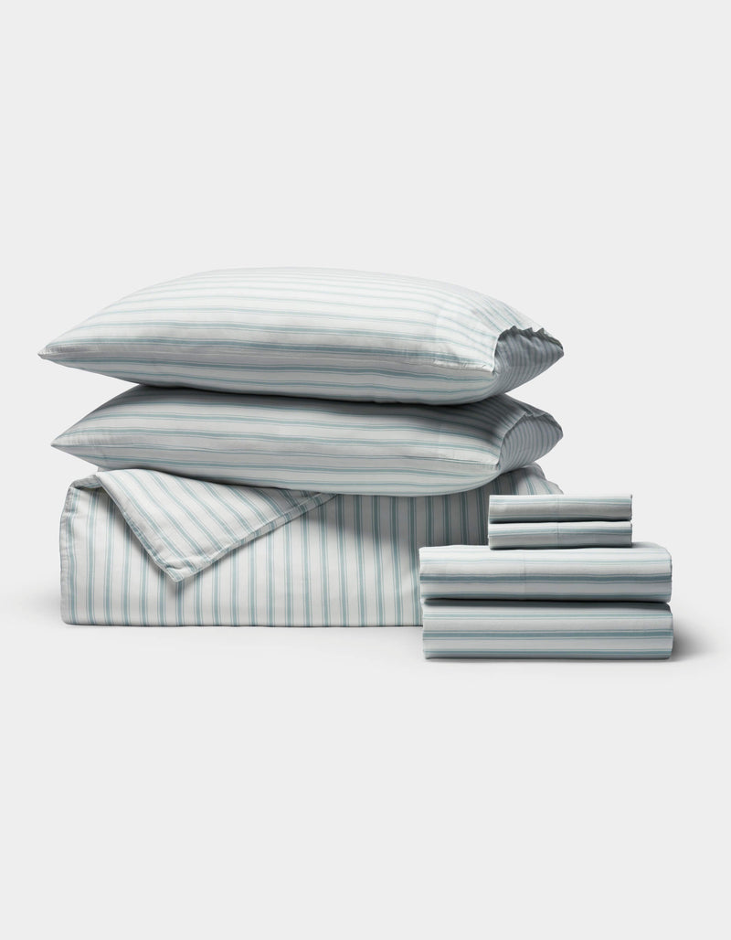 A neatly arranged stack of Cozy Earth's Soft-Wash Cotton Bedding Core Bundle, including pillows, a comforter, and folded sheets in white and light blue, displayed on a plain white background.