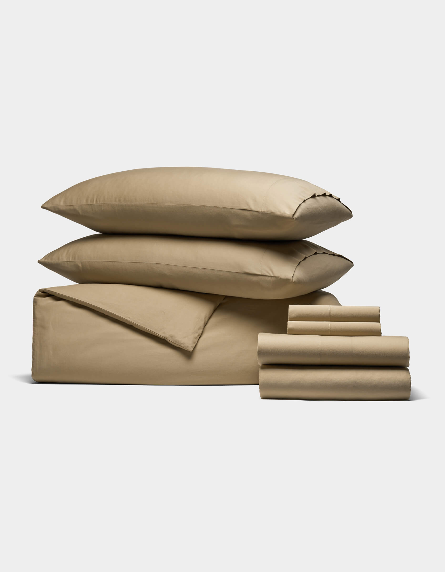 The Soft-Wash Cotton Bedding Core Bundle by Cozy Earth, featuring a tan duvet, flat and fitted sheets, pillowcases, and two stacked pillows, is neatly folded and displayed on a plain white background.