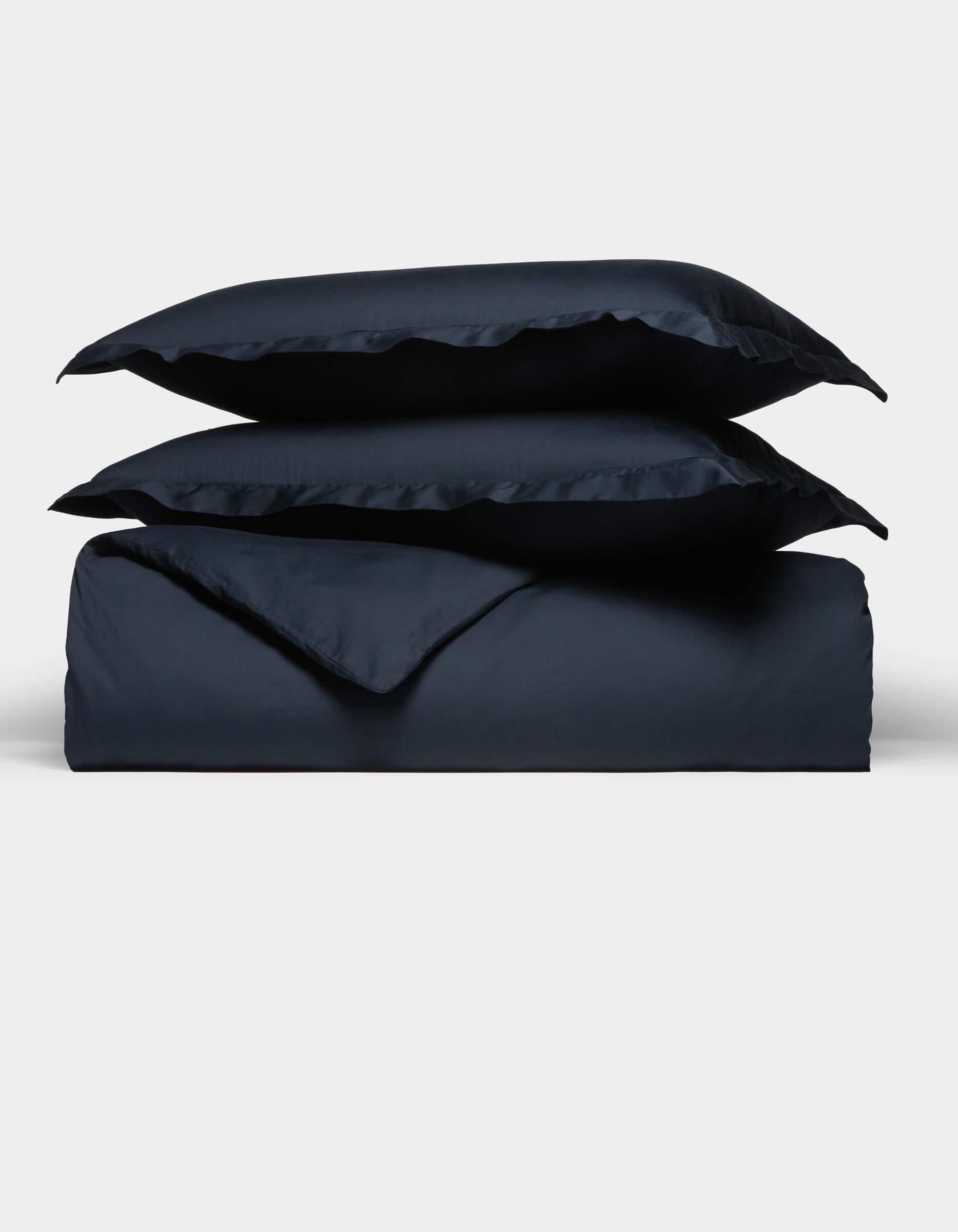 The Cozy Earth Soft-Wash Cotton Duvet Set, in navy blue, features two pillows placed atop a neatly folded duvet, all displayed against a plain white background.|Color:Eclipse