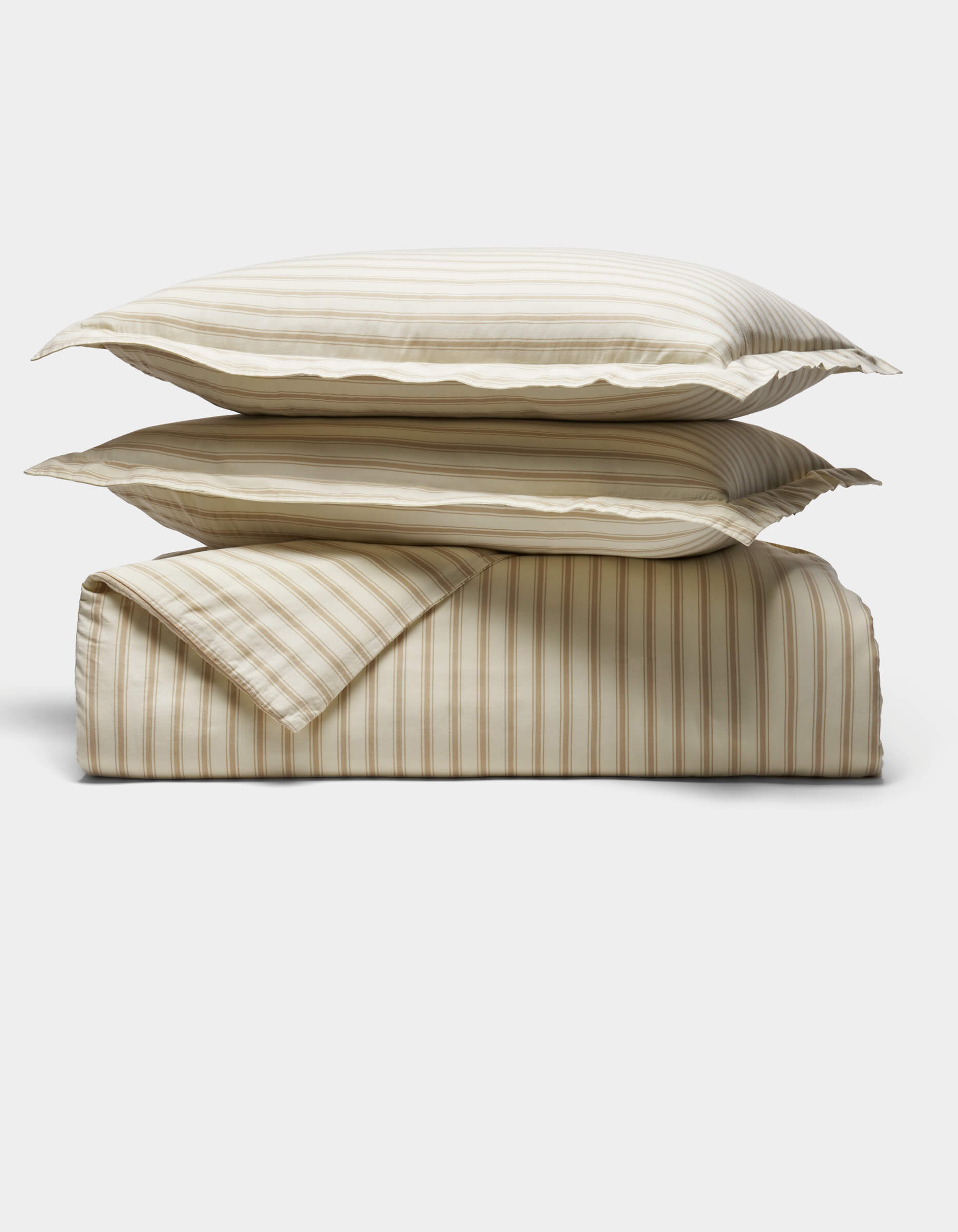Two striped pillows rest atop a folded matching duvet from the Soft-Wash Cotton Duvet Set by Cozy Earth, all in beige and white tones, set against a plain white background.