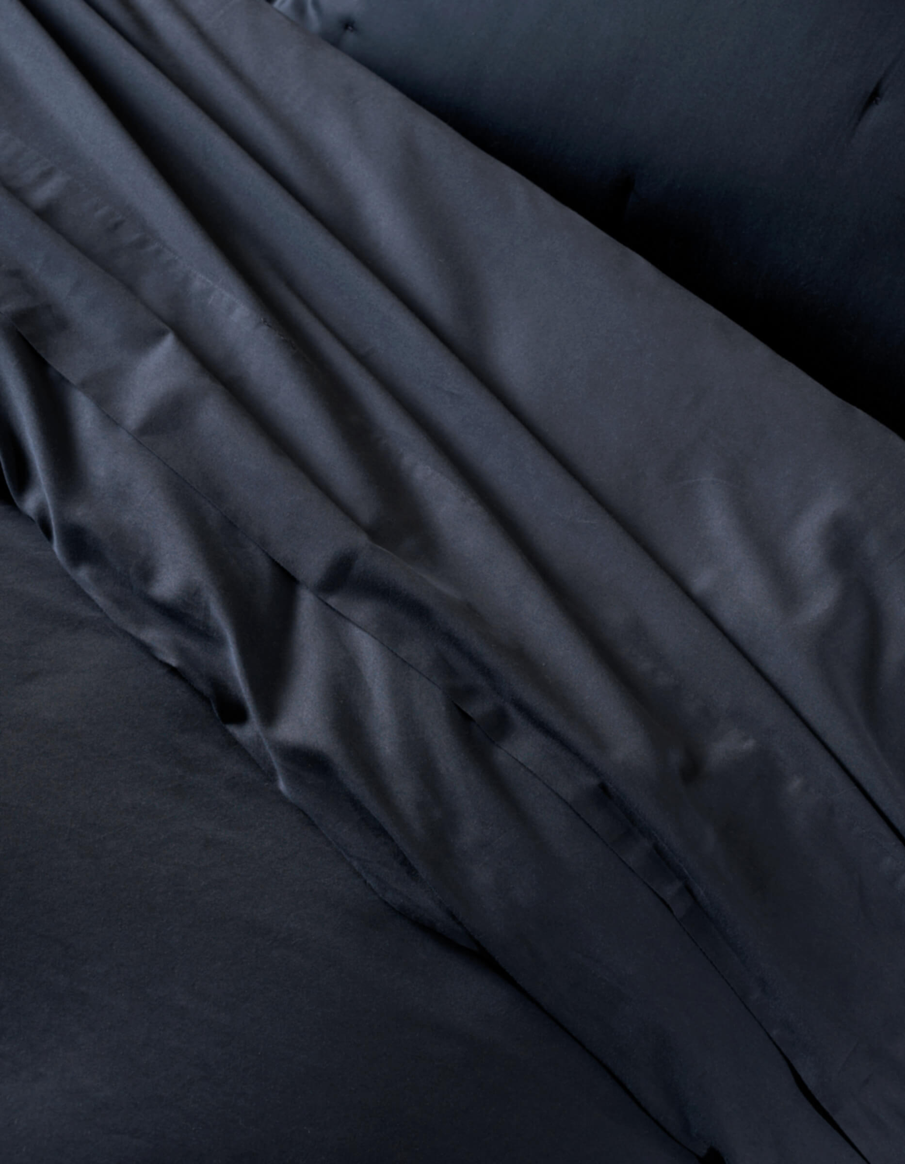 A close-up of the Cozy Earth Soft-Wash Cotton Duvet Cover shows neatly arranged black bedding and pillowcases, highlighting the smooth, slightly shiny fabric with gentle folds and creases.