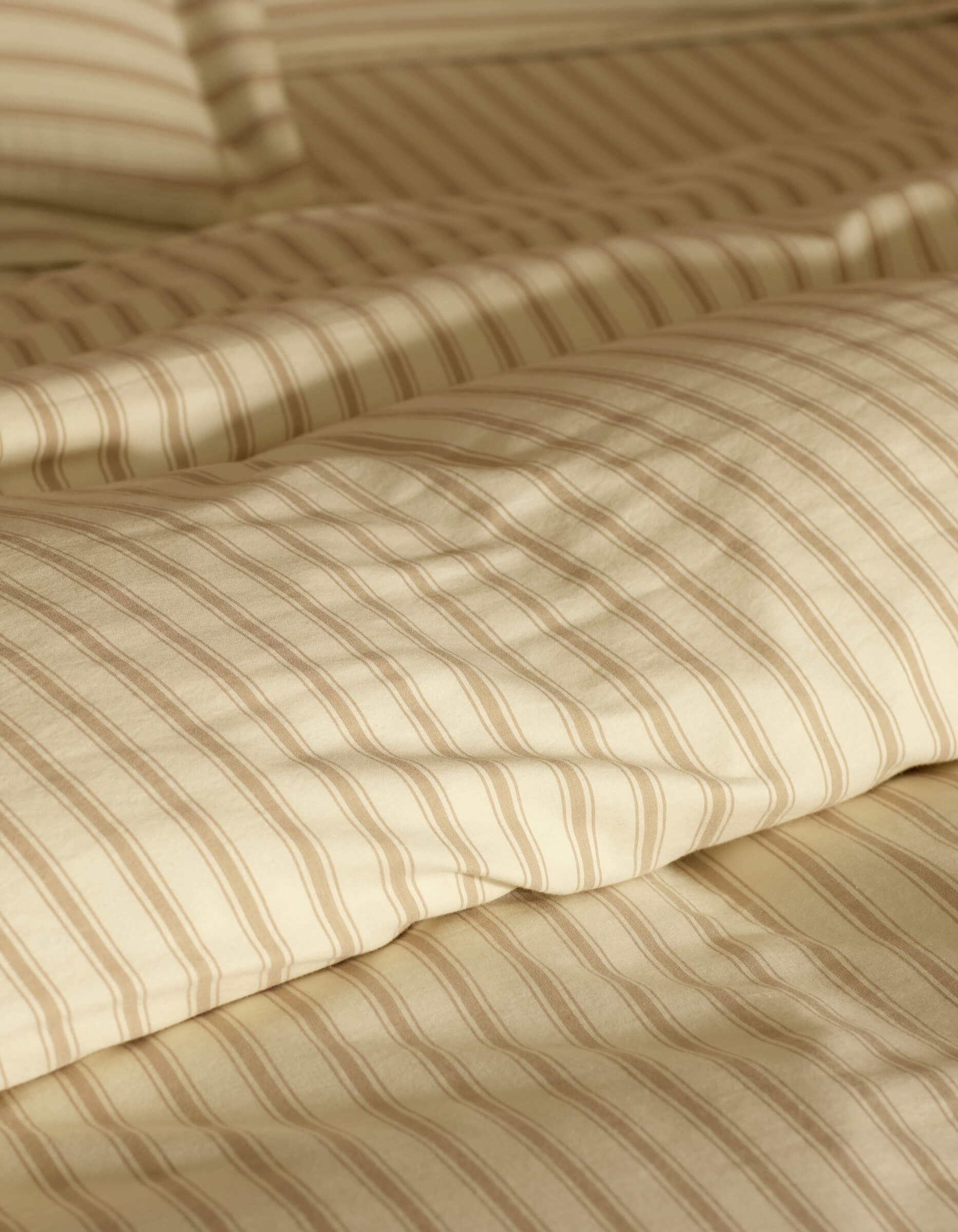 Close-up of a neatly made bed featuring Cozy Earth's Soft-Wash Cotton Duvet Cover in cream and beige stripes, with a matching pillow, softly lit to accentuate the smooth fabric texture.
