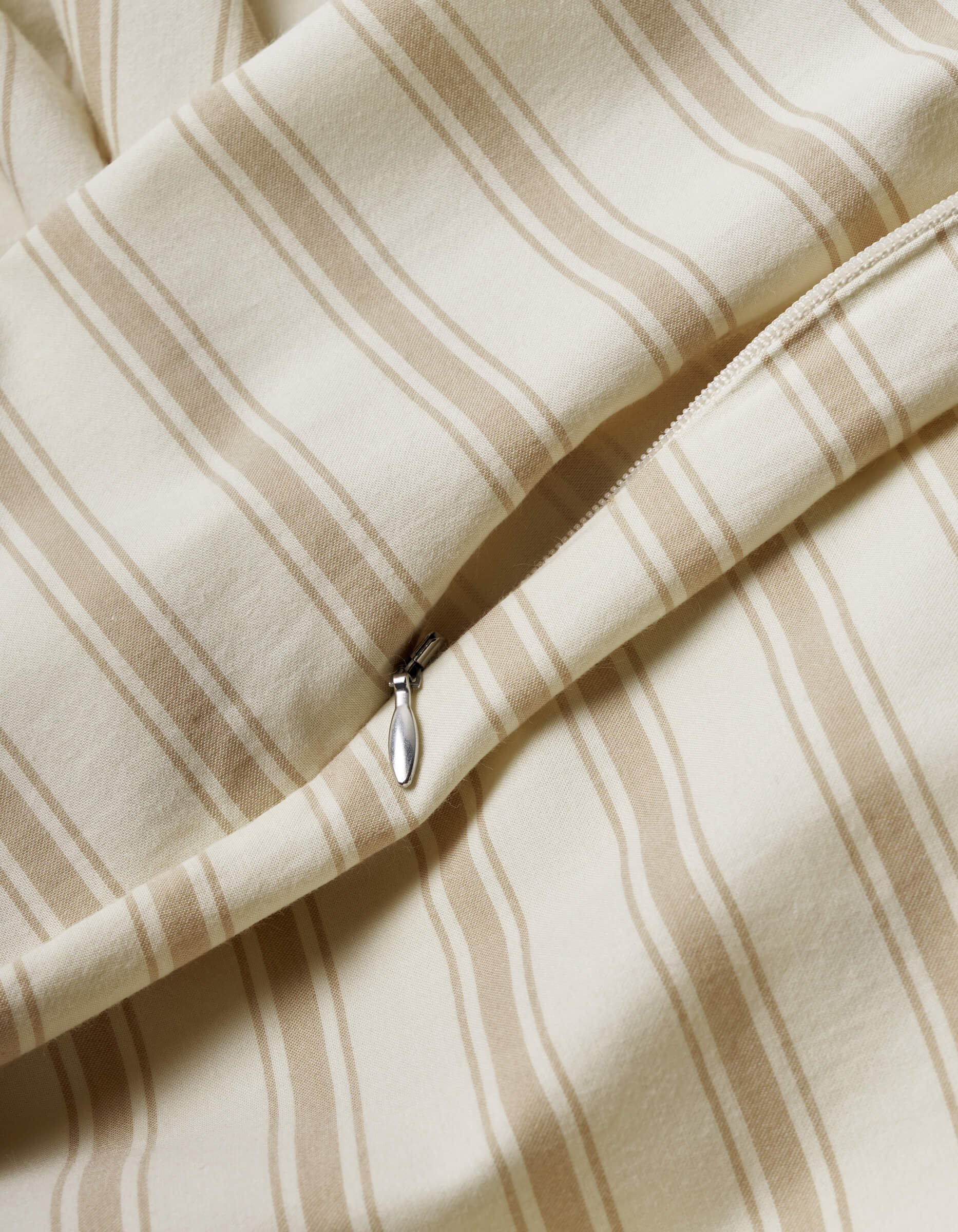 A close-up of the Cozy Earth Soft-Wash Cotton Duvet Cover shows beige and cream vertical stripes, a smooth texture, and a partially open visible zipper.