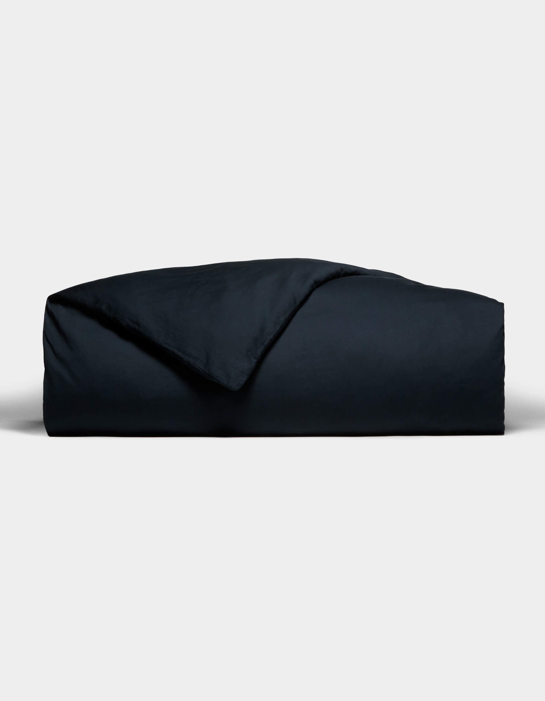 The Cozy Earth Soft-Wash Cotton Duvet Cover, in a dark hue, is neatly folded with one corner flipped to reveal its smooth texture, set against a plain light gray background.