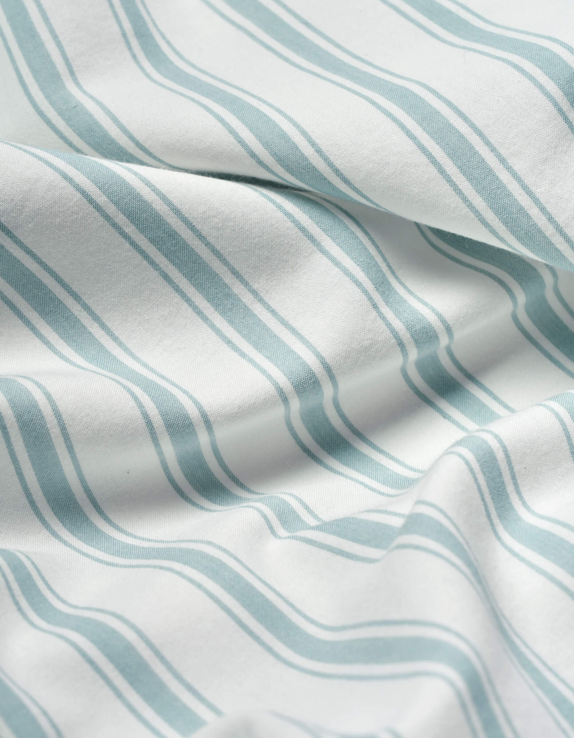 Close-up of Cozy Earth’s Soft-Wash Cotton Sheet Set in white, featuring light blue wavy parallel stripes. The soft fabric is slightly wrinkled, forming gentle folds and subtle shadows.