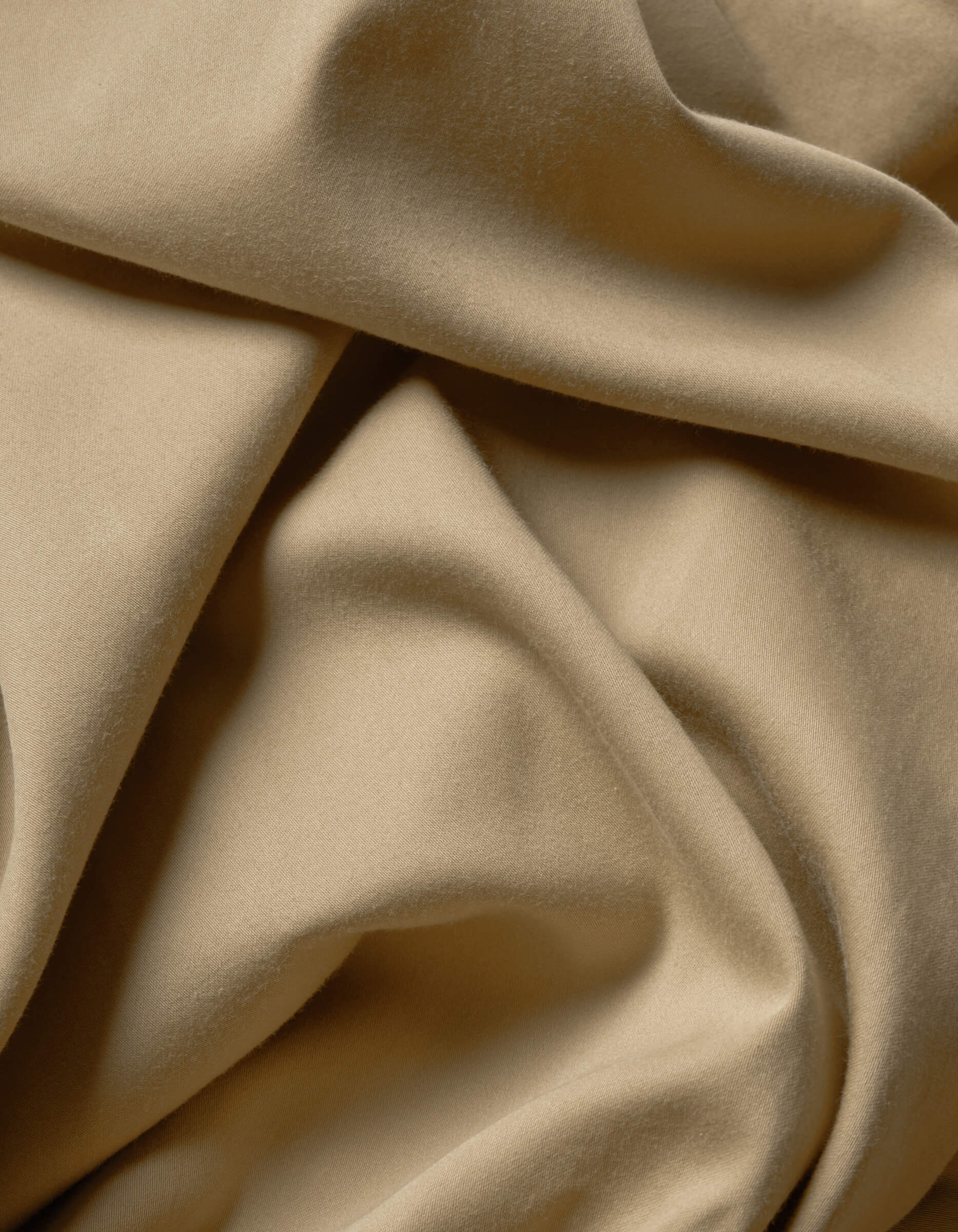 A close-up of Cozy Earth's Soft-Wash Cotton Flat Sheet showcases its soft beige fabric with smooth folds and gentle shadows, highlighting the luxurious texture and movement.