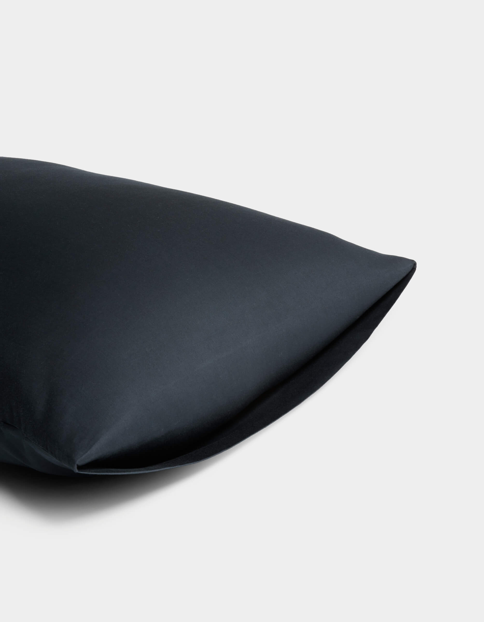 A close-up showcases the Soft-Wash Cotton Pillowcase by Cozy Earth in black, made from smooth fabric, set against a plain light gray background. Only part of the pillowcase appears on the left side of the image.