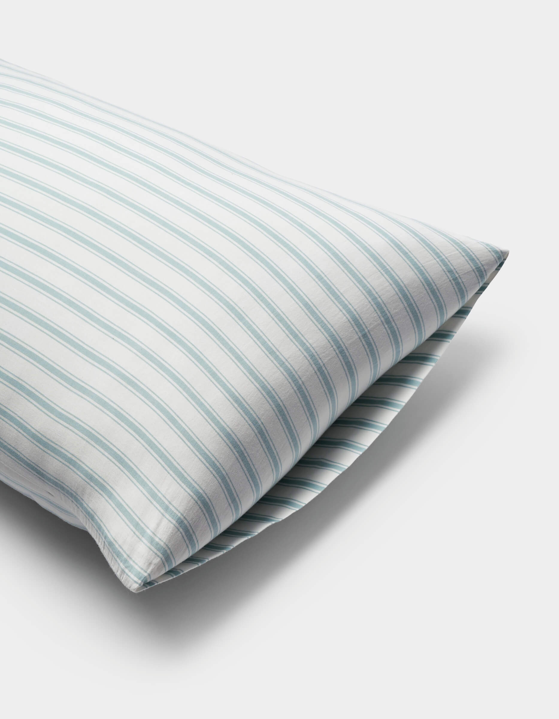 A close-up of a Cozy Earth Soft-Wash Cotton Pillowcase with a white cover and light blue and green vertical stripes, set against a plain white background.