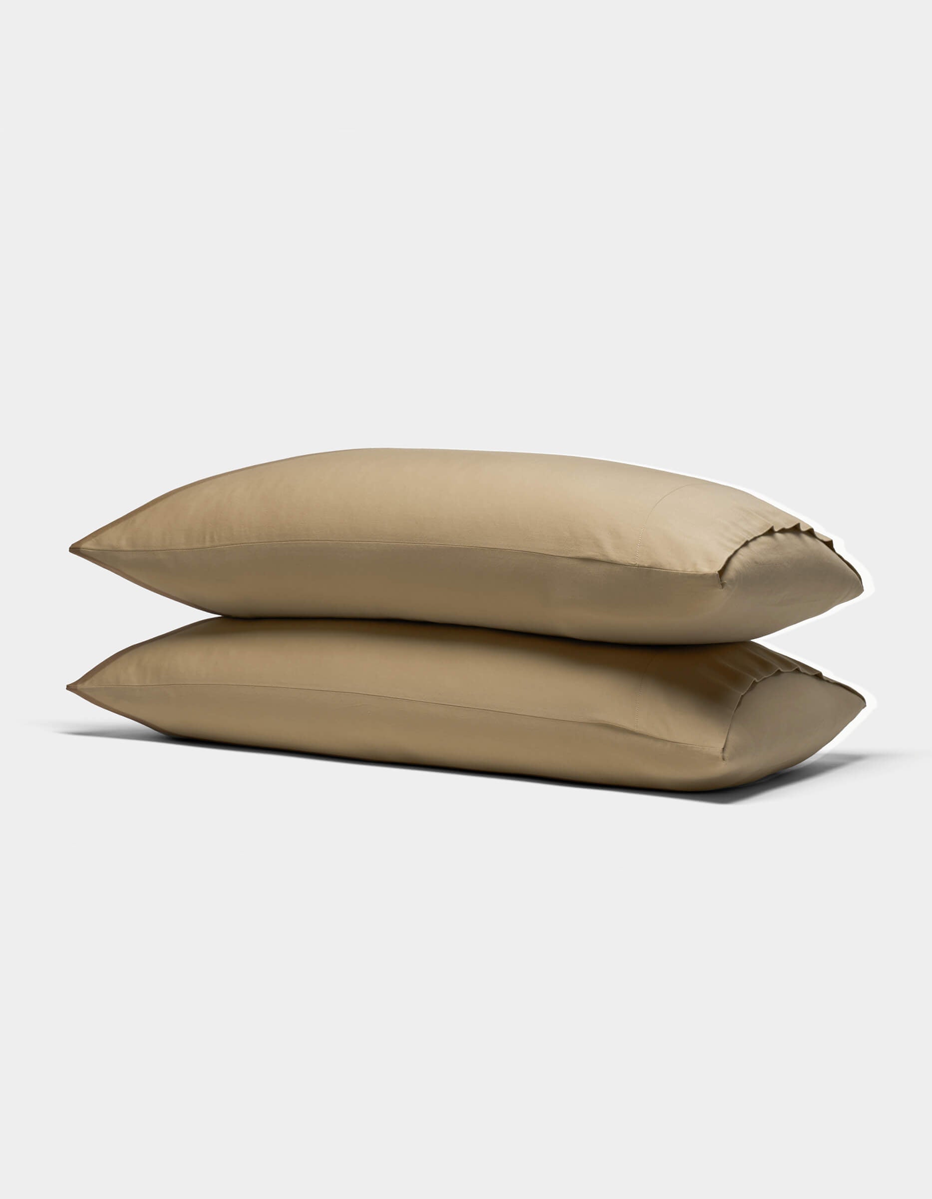 Two Cozy Earth Soft-Wash Cotton Pillowcases in light brown are stacked against a plain white background, showcasing their smooth texture and plush, comfortable appearance.