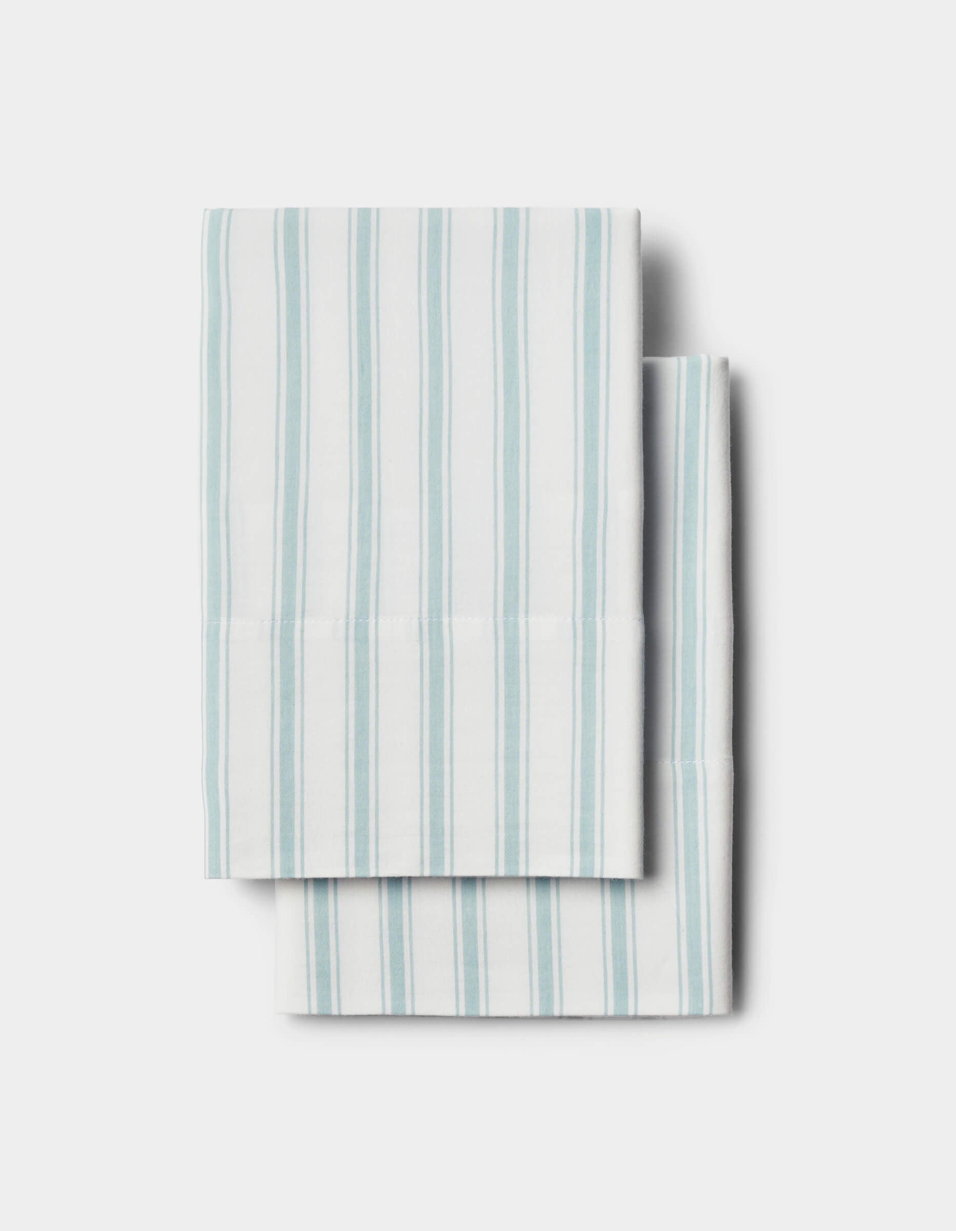 Two Soft-Wash Cotton Pillowcases by Cozy Earth, white with vertical light blue stripes, neatly folded and stacked on a plain light background.