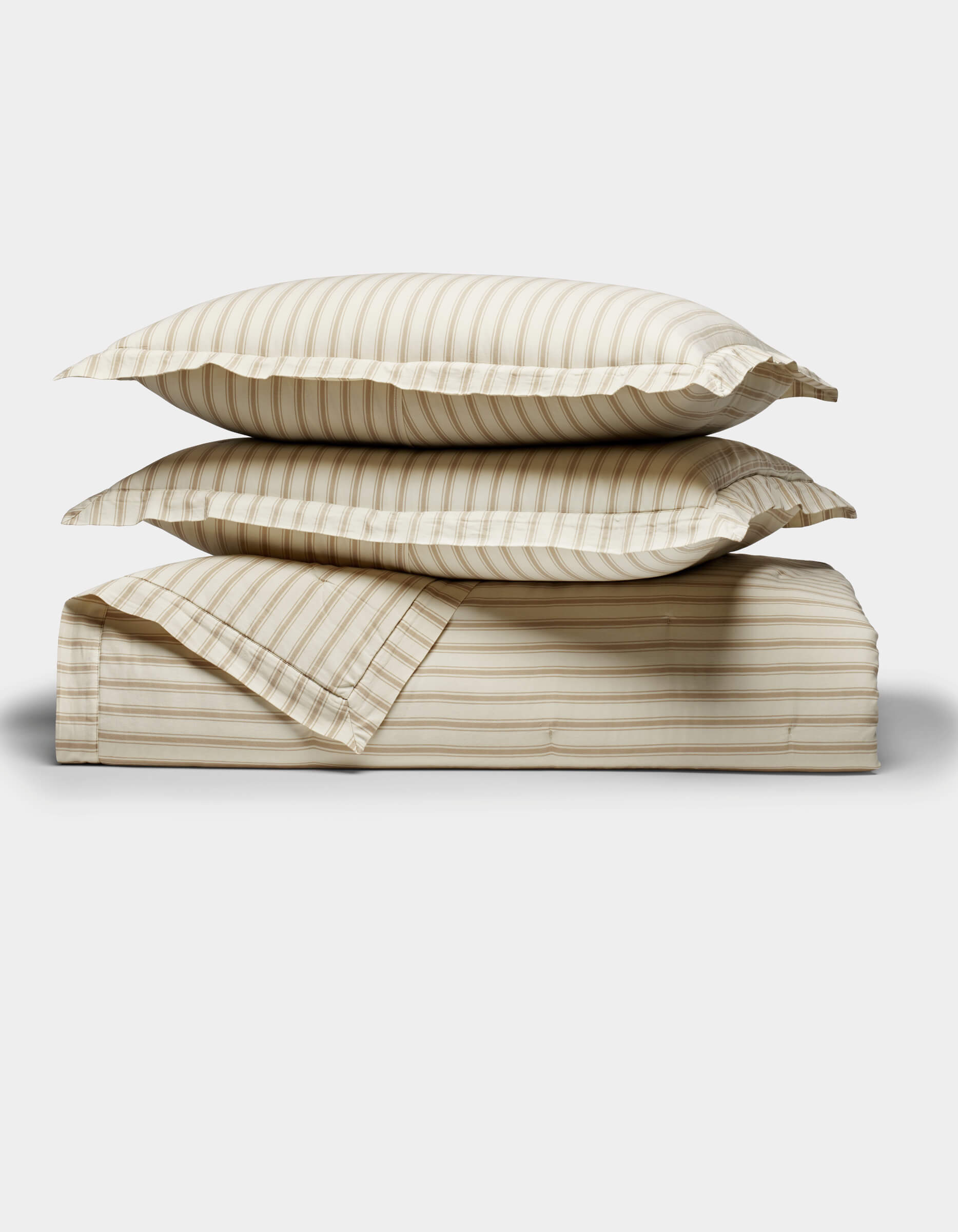 Two beige and cream striped Soft-Wash Cotton Quilt Set pillows by Cozy Earth are stacked on a matching folded sheet, displayed against a plain white background.