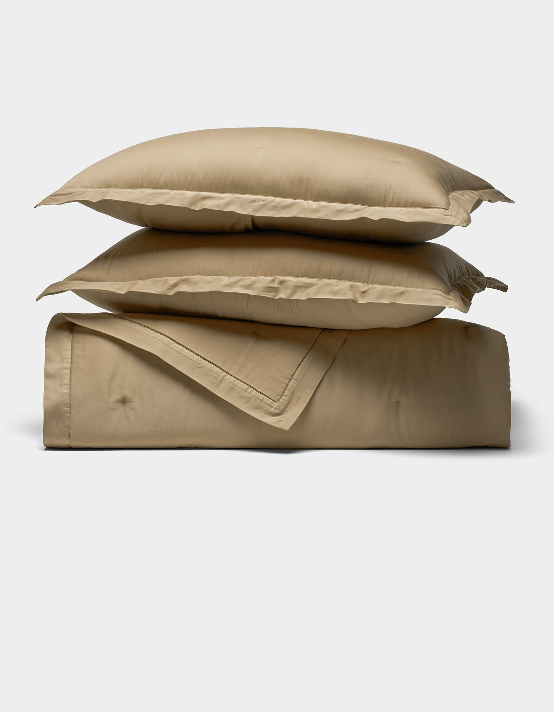 The Soft-Wash Cotton Quilt Set by Cozy Earth features two beige pillows stacked atop a matching folded comforter, displayed against a plain, light background.