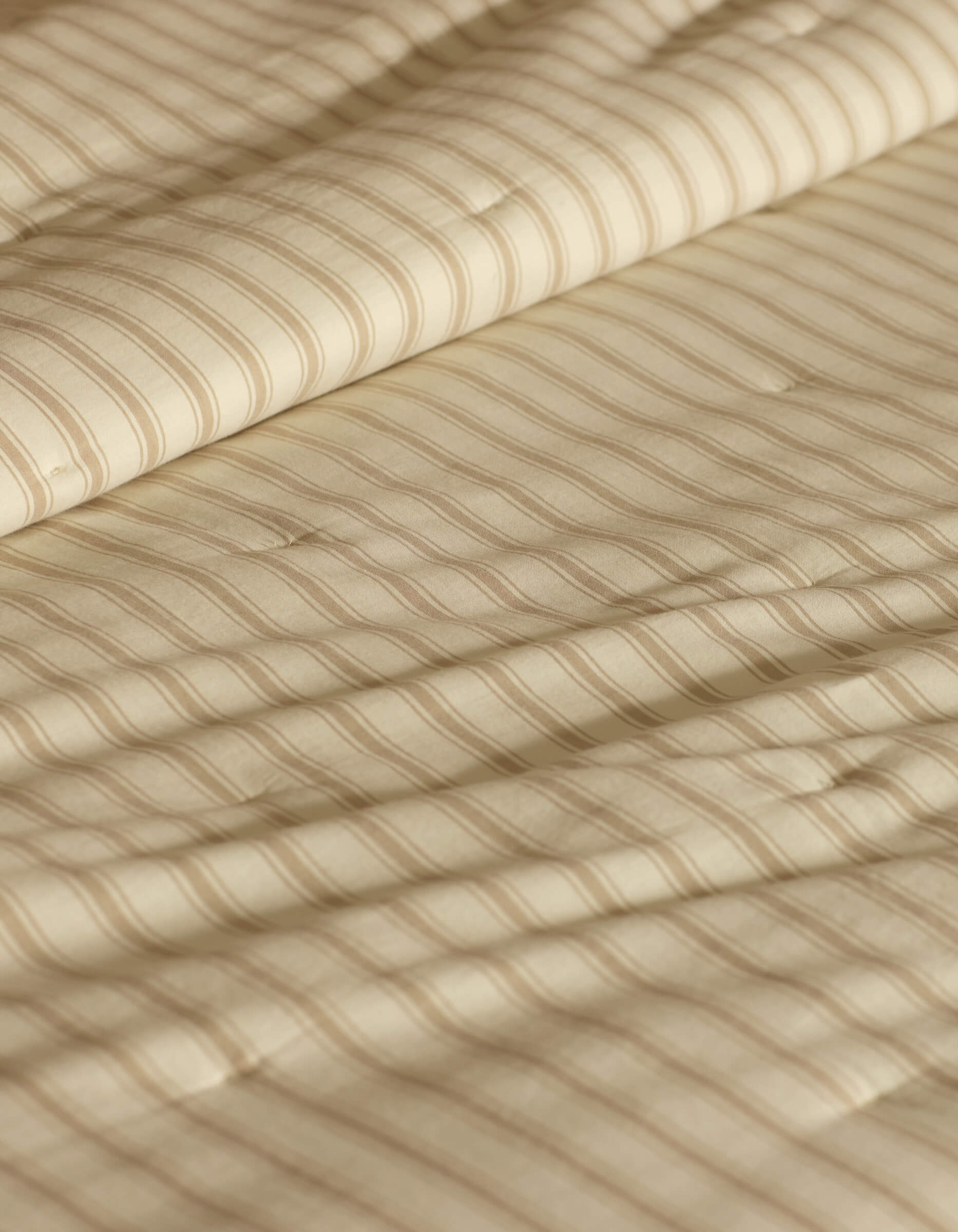 A close-up of the Cozy Earth Soft-Wash Cotton Quilt in beige shows its quilted fabric with thin horizontal stripes and gentle folds, highlighting its soft, textured look.