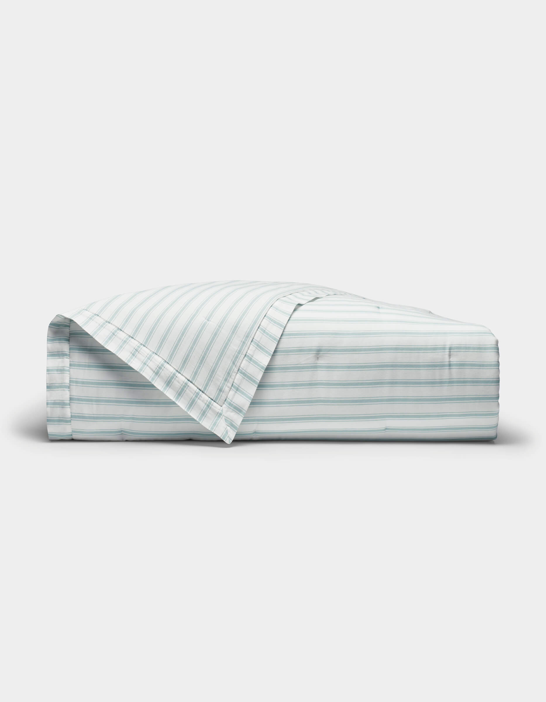 The Cozy Earth Soft-Wash Cotton Quilt is shown neatly folded with one corner turned back, revealing its light color and thin horizontal blue and gray stripes against a plain white background.|Color:River and Sea Salt Stripe