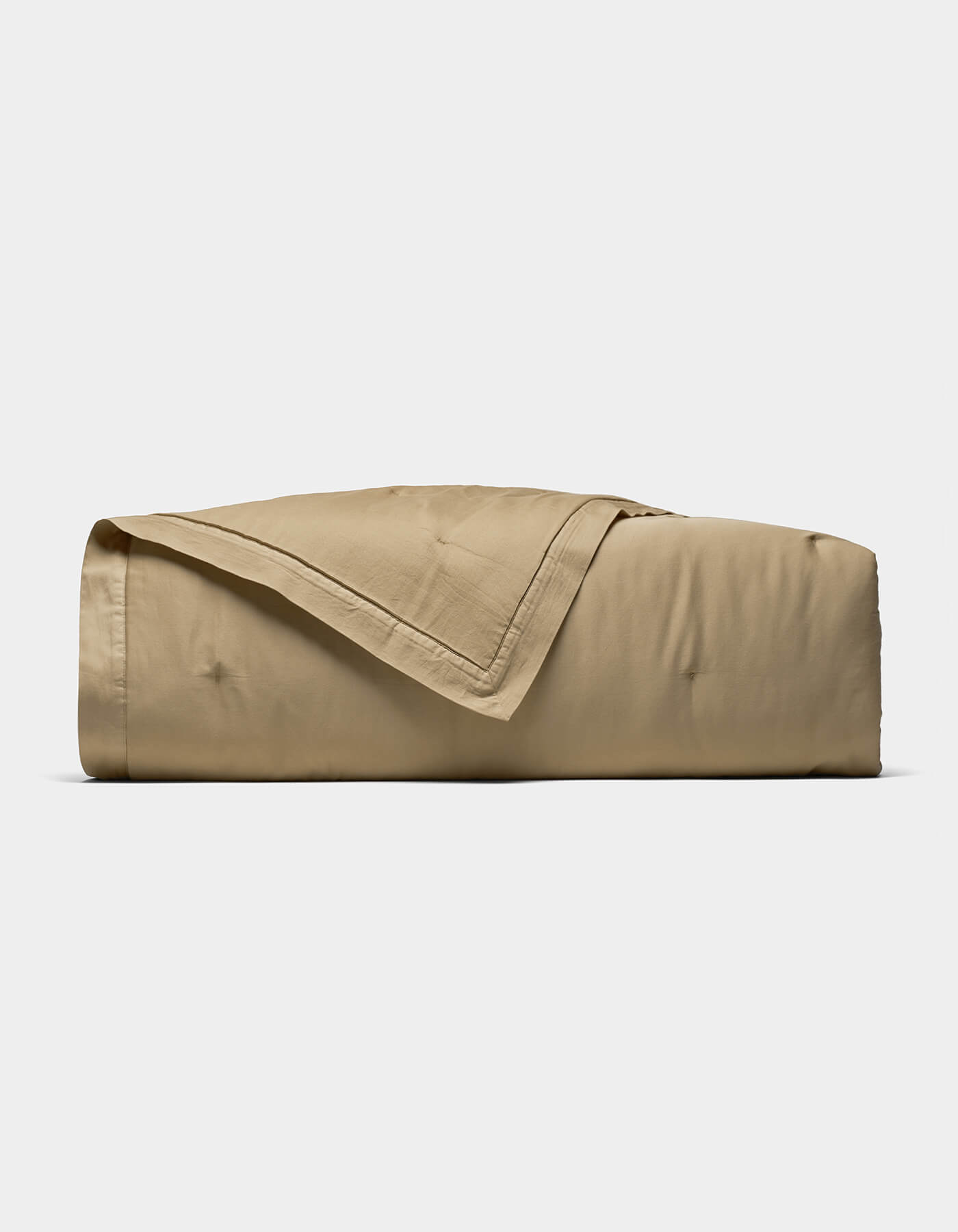 The Cozy Earth Soft-Wash Cotton Quilt, in light brown, is neatly folded with one corner draped over the top and displayed on a plain white background.