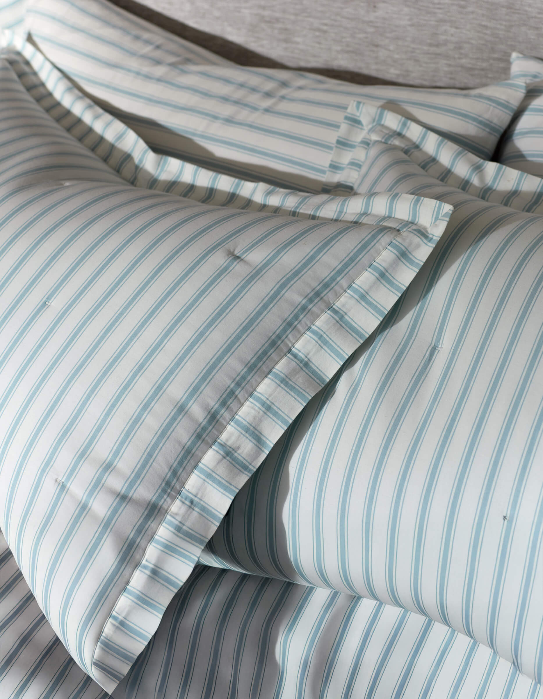 Close-up of Cozy Earth's Soft-Wash Cotton Quilted Shams, neatly arranged with light blue and white vertical stripes, ruffled pillowcase edges, and a soft, textured background.