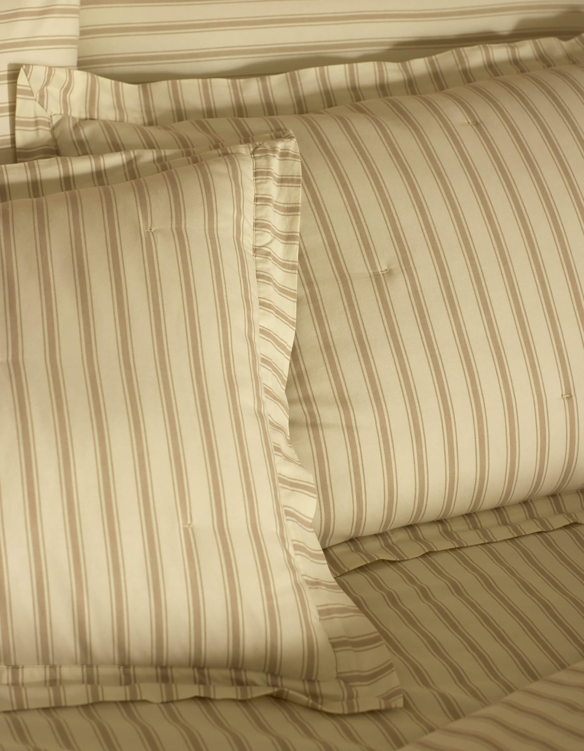 Close-up of a neatly made bed featuring Cozy Earth Soft-Wash Cotton Quilted Shams, showcasing smooth, soft fabric and subtle beige and light brown stripes on pillows and sheets for a cozy look.
